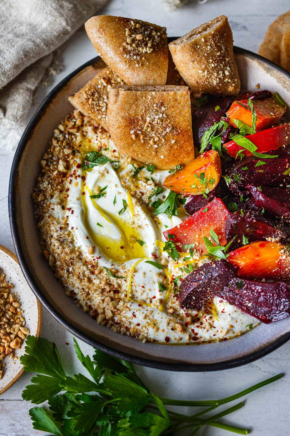 creamy whipped feta in dish topped with olive oil, lemon zest, parsley, dukkah, and roasted beets, served with pita.