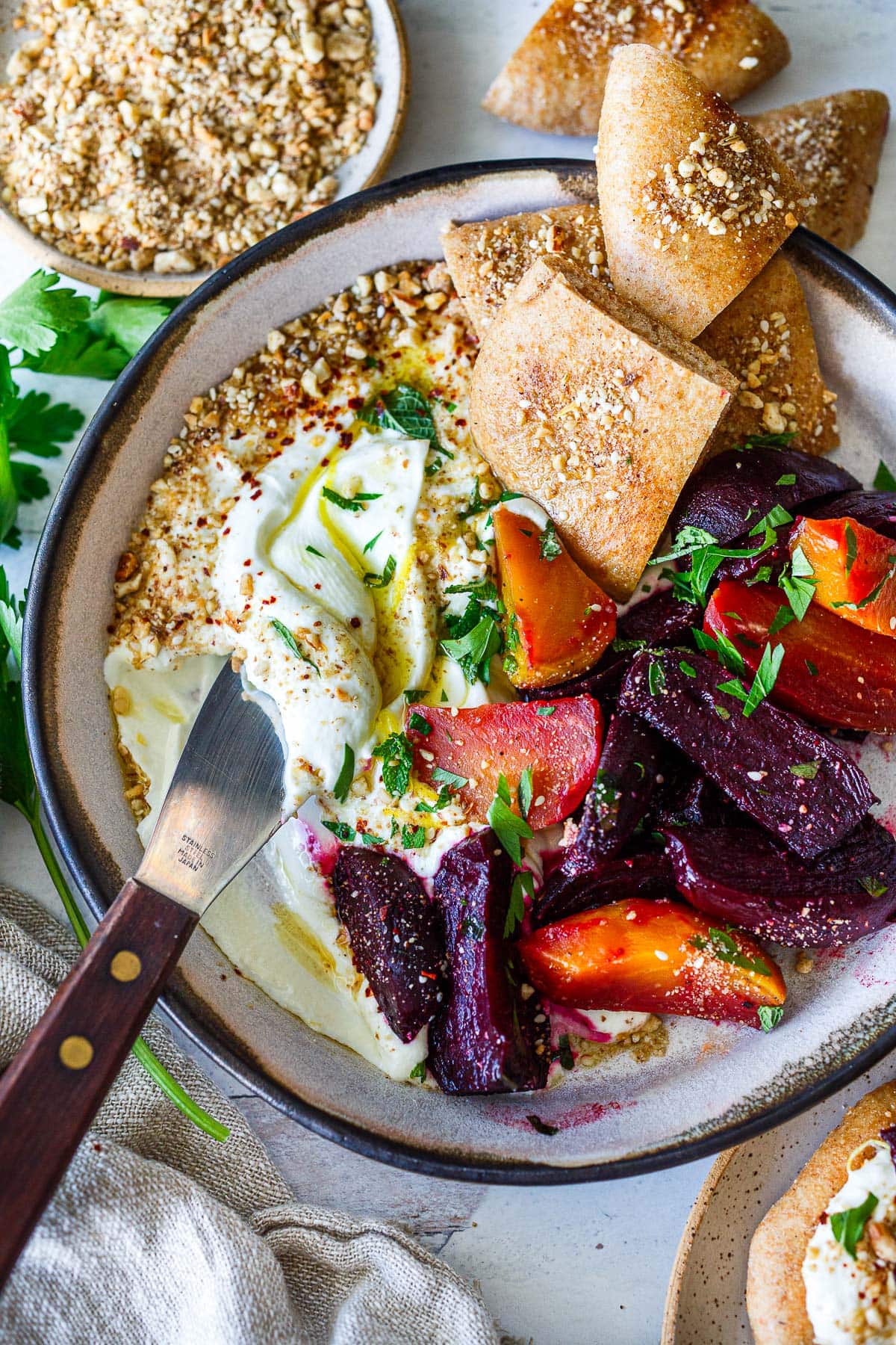 serving dish with whipped feta, topped with olive oil, lemon zest, parsley, dukkah, roasted beets, and pita, with serving knife.