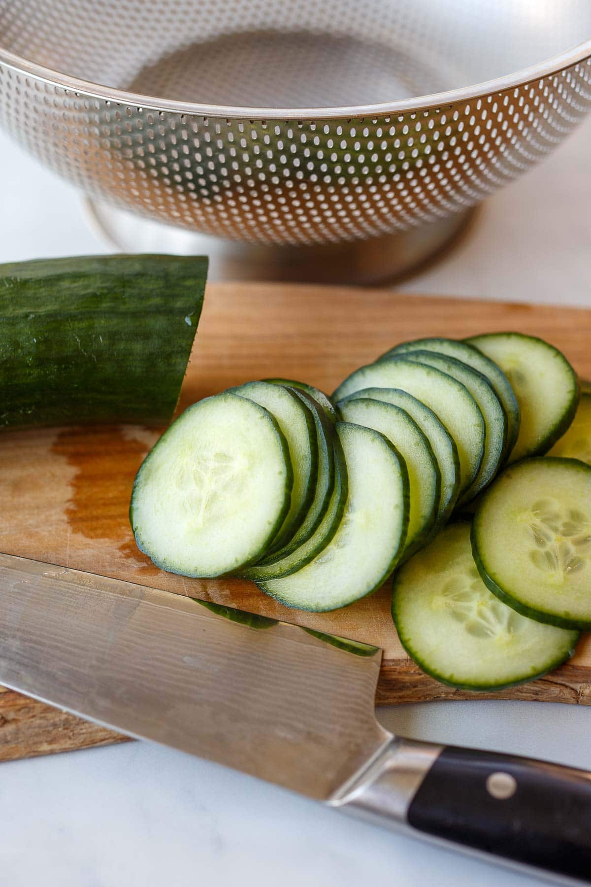knife and wood board with thin cucumber slices.