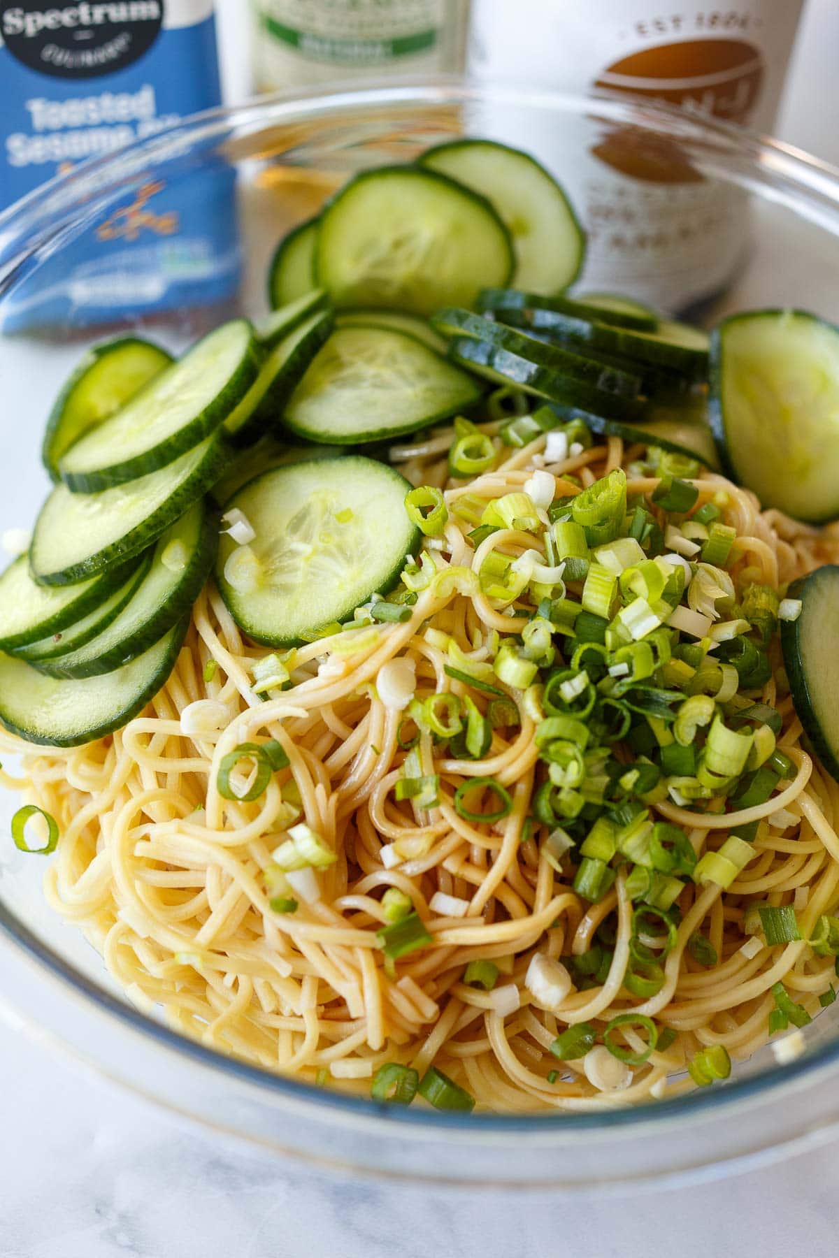 large mixing bowl with cooked ramen noodles, green onions, and sliced cucumbers.