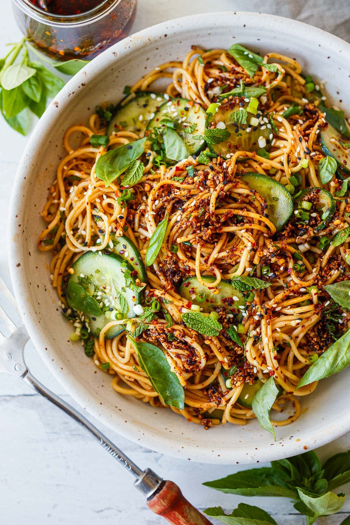 bowl with cold noodle salad with sliced cucumbers, fresh herbs, green onions, and chili crisp.