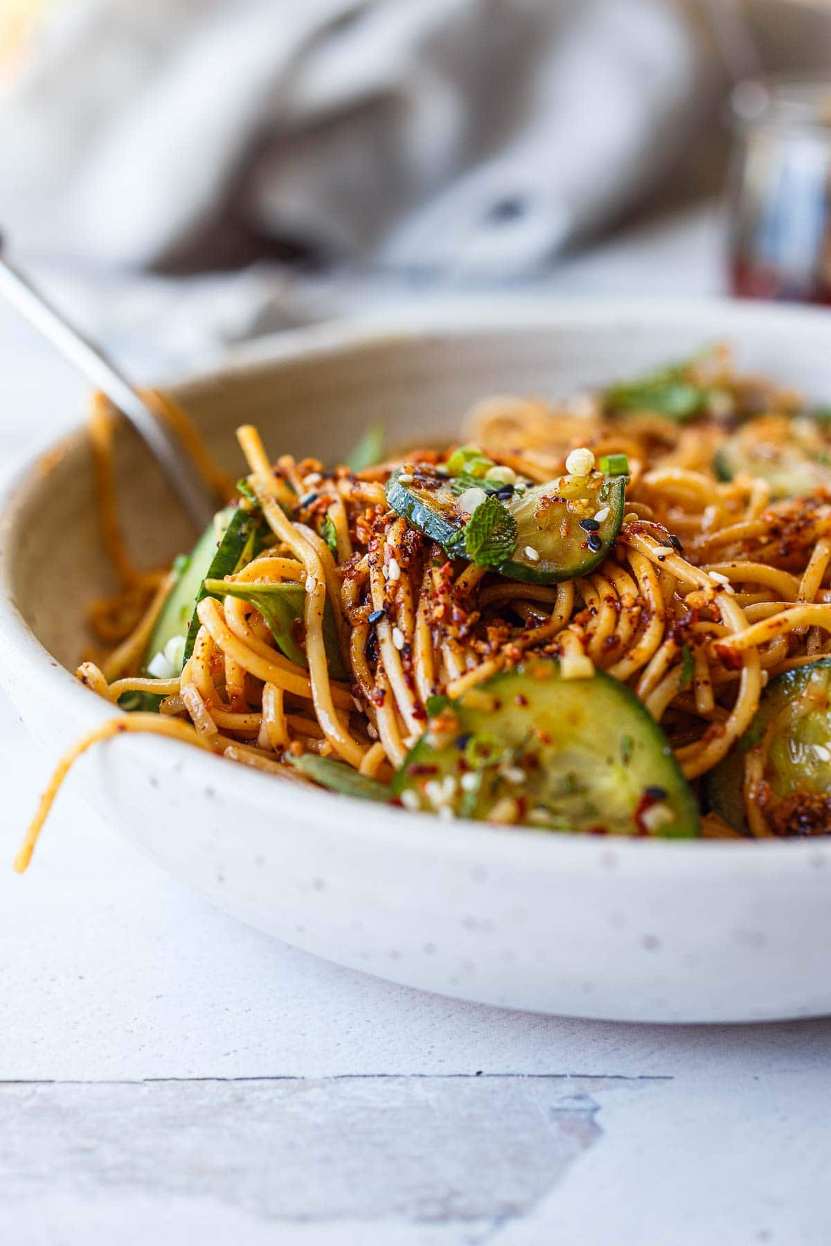 serving bowl with close up cold noodle salad mixed with cucumbers, mint, and green onions, topped with chili crisp.