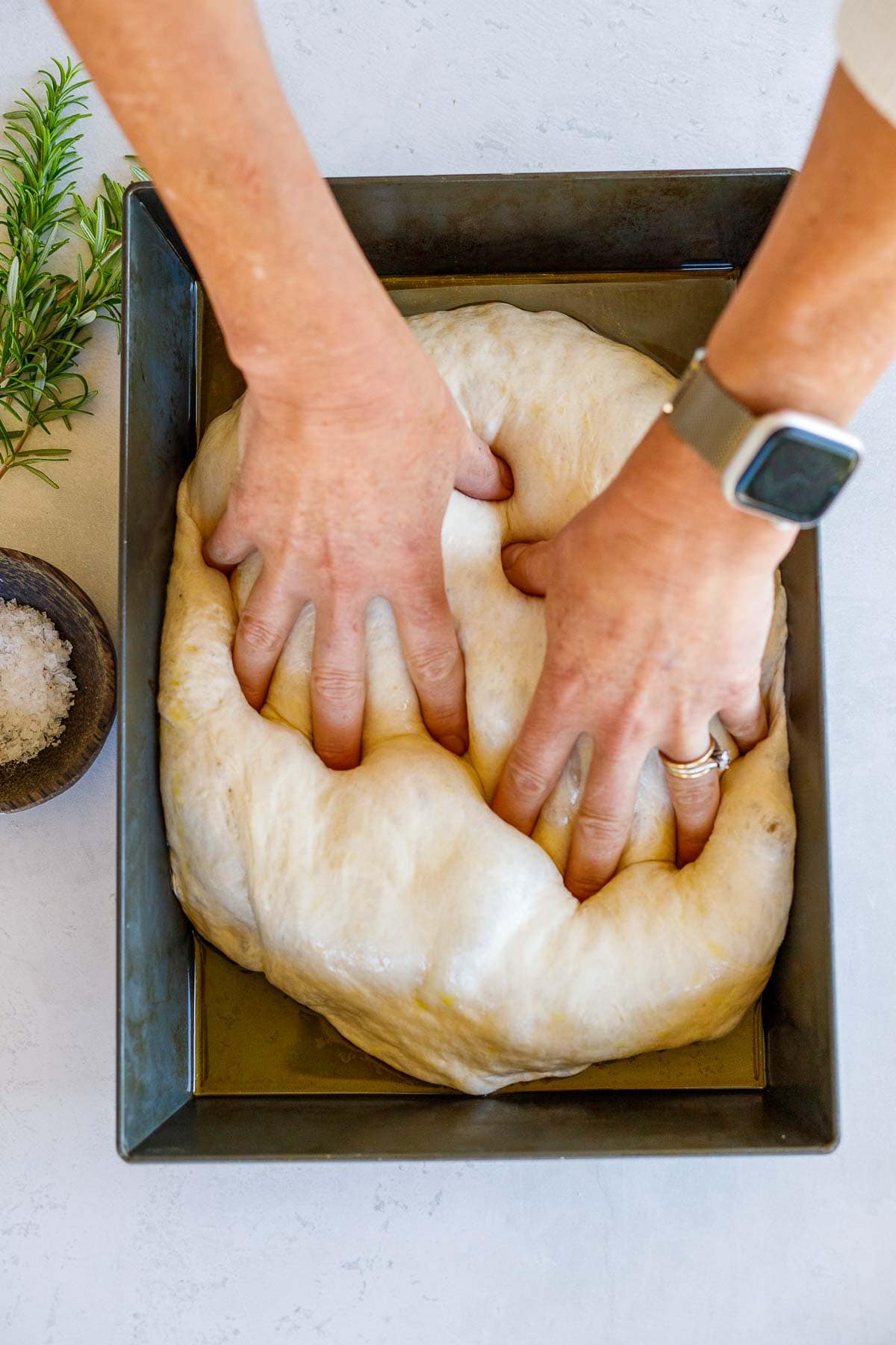hands poking holes into the focaccia dough.