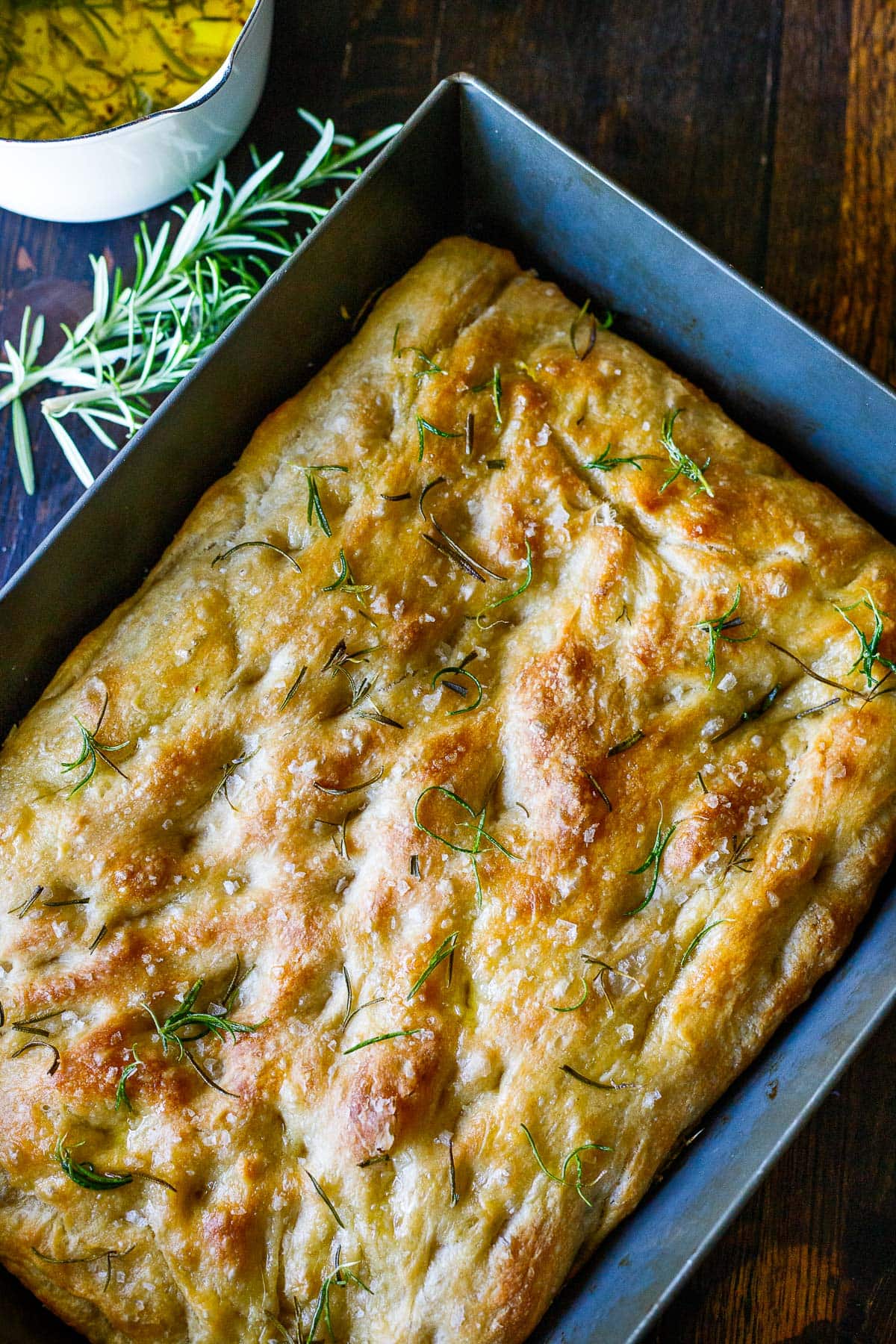 baked focaccia bread in pan topped with rosemary and salt.