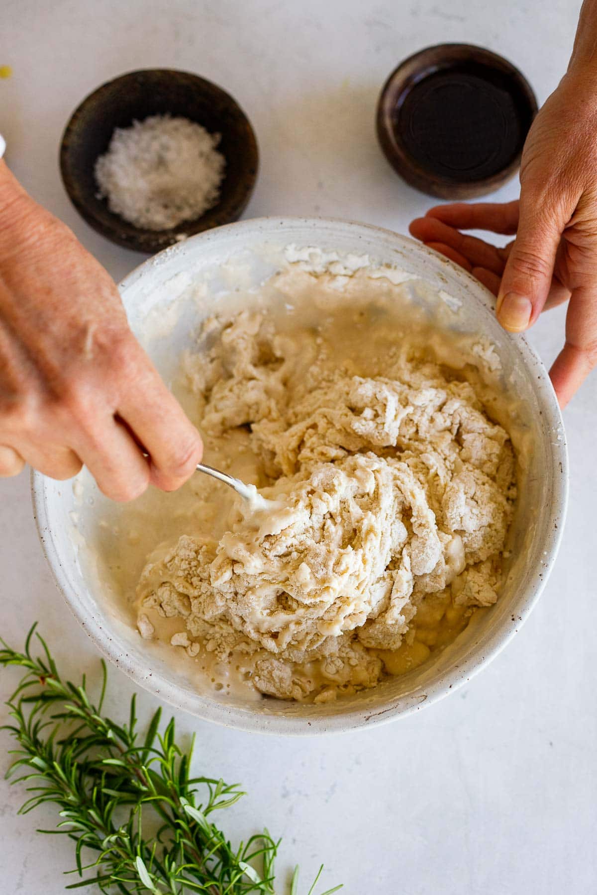 hands holding bowl and using fork to mix flour and water into dough.