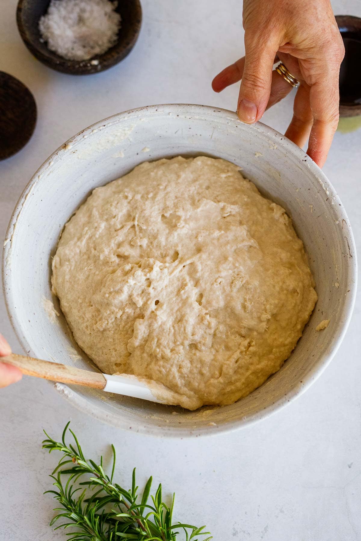 hands holding bowl and using spatula to scrape down the edges of the bowl to create a dough ball.