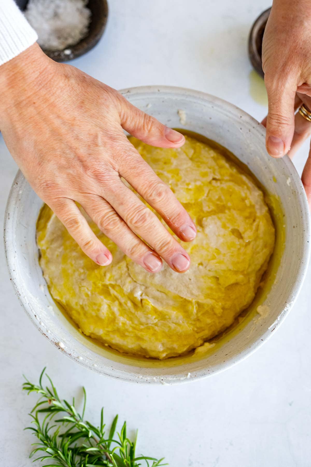 using hands to spread olive oil evenly over dough.