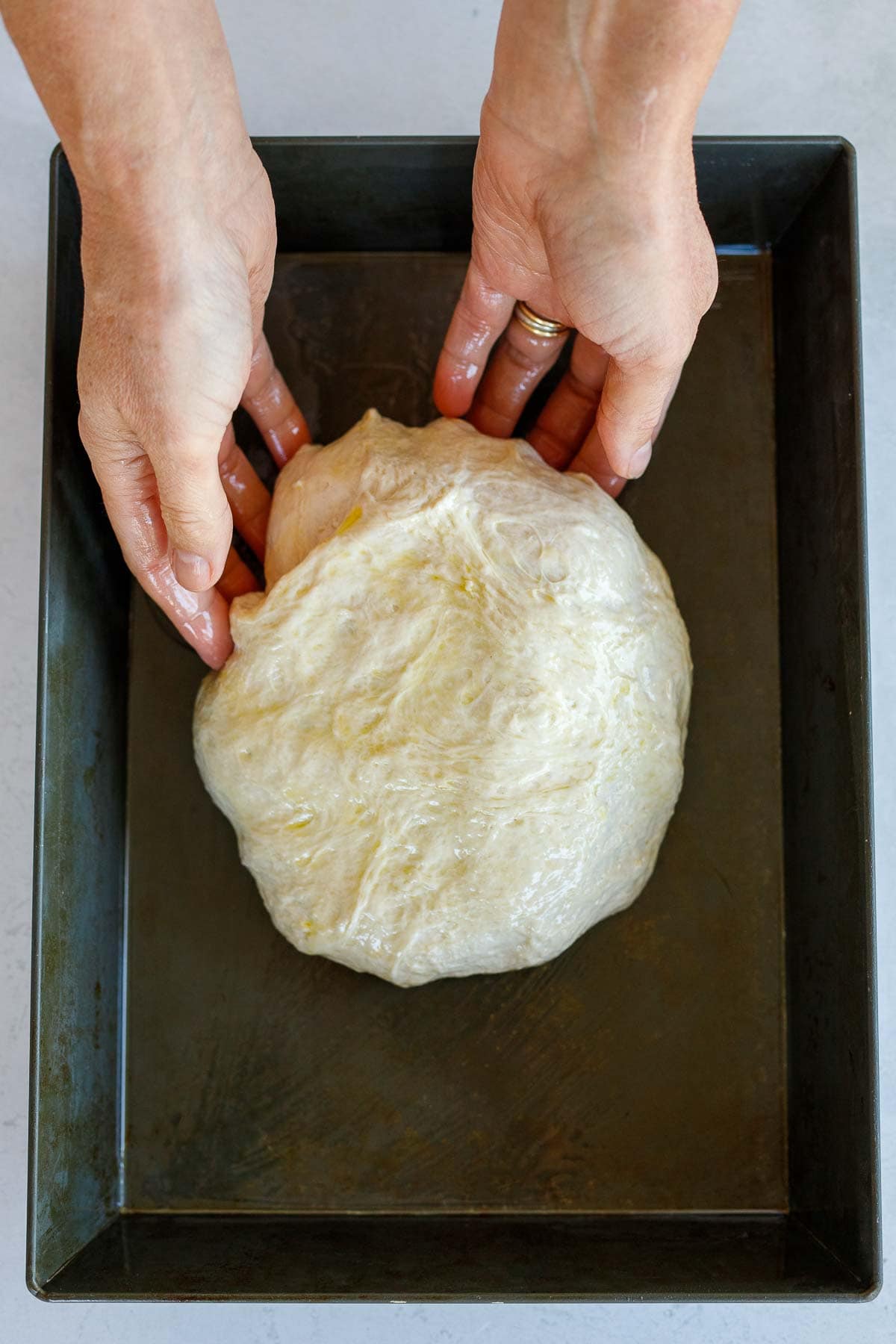 hands transferring focaccia dough ball to sheet pan.