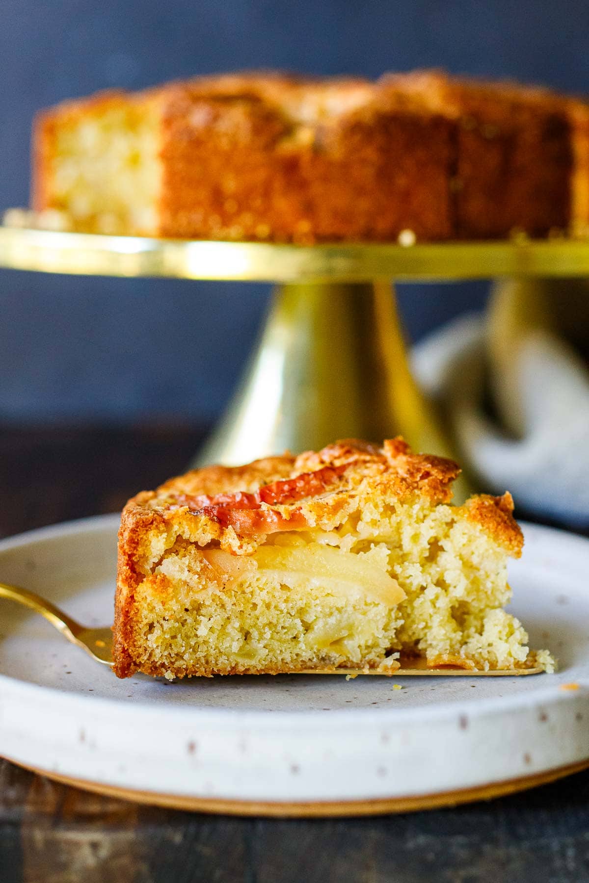 plate with slice of apple cake showing moist interior and crackly top layer with apple slices. 