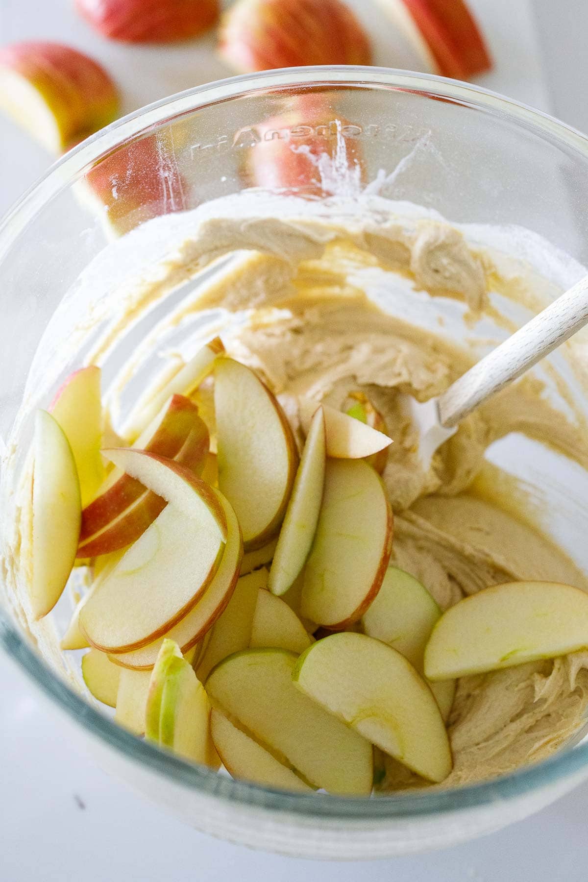 glass mixing bowl with apple cake batter and apple slices. 