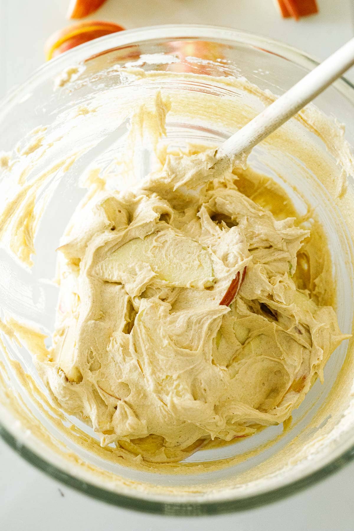 glass mixing bowl with apple cake batter and spatula folding in the apple slices. 