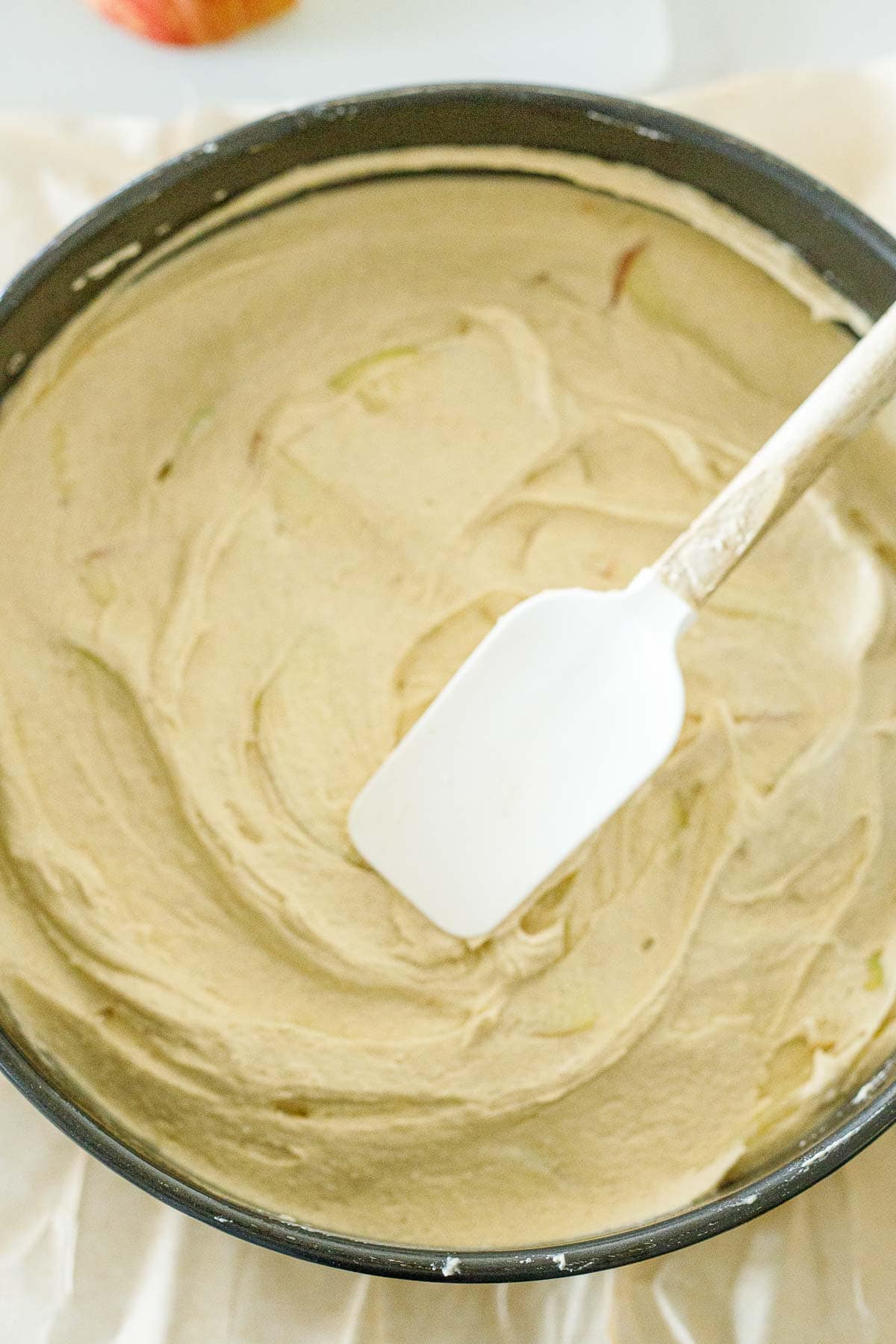 spatula smoothing out the top layer of the apple cake batter in springform pan. 