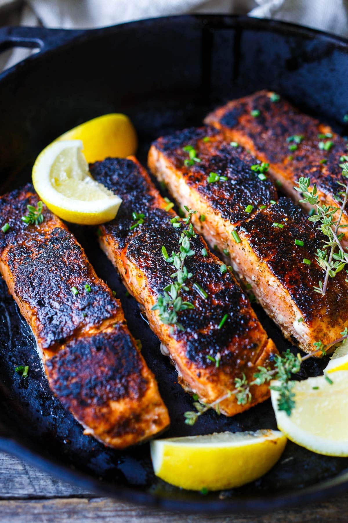 blackened salmon filets in cast iron skillet with fresh herbs and lemon wedges.