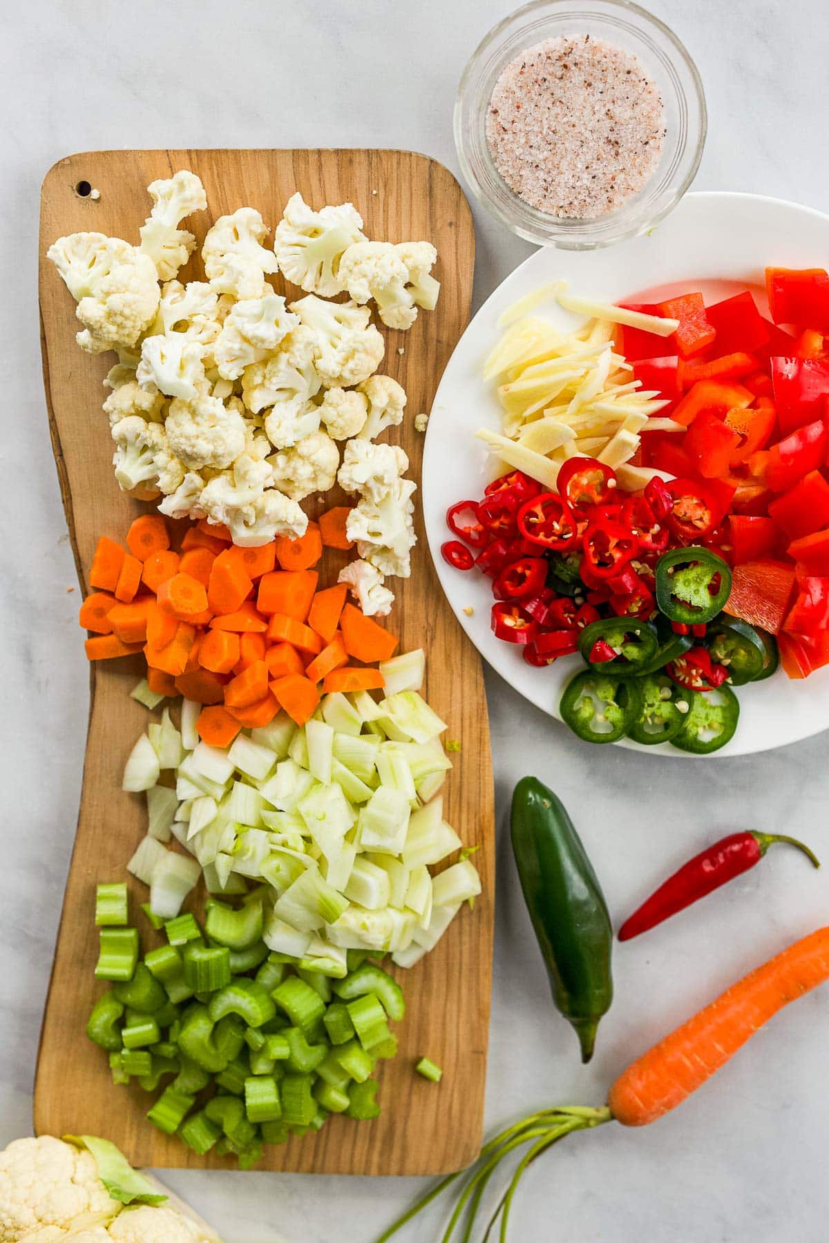 wood board with bite size veggies next to plate with more chopped veggies and sliced peppers. 