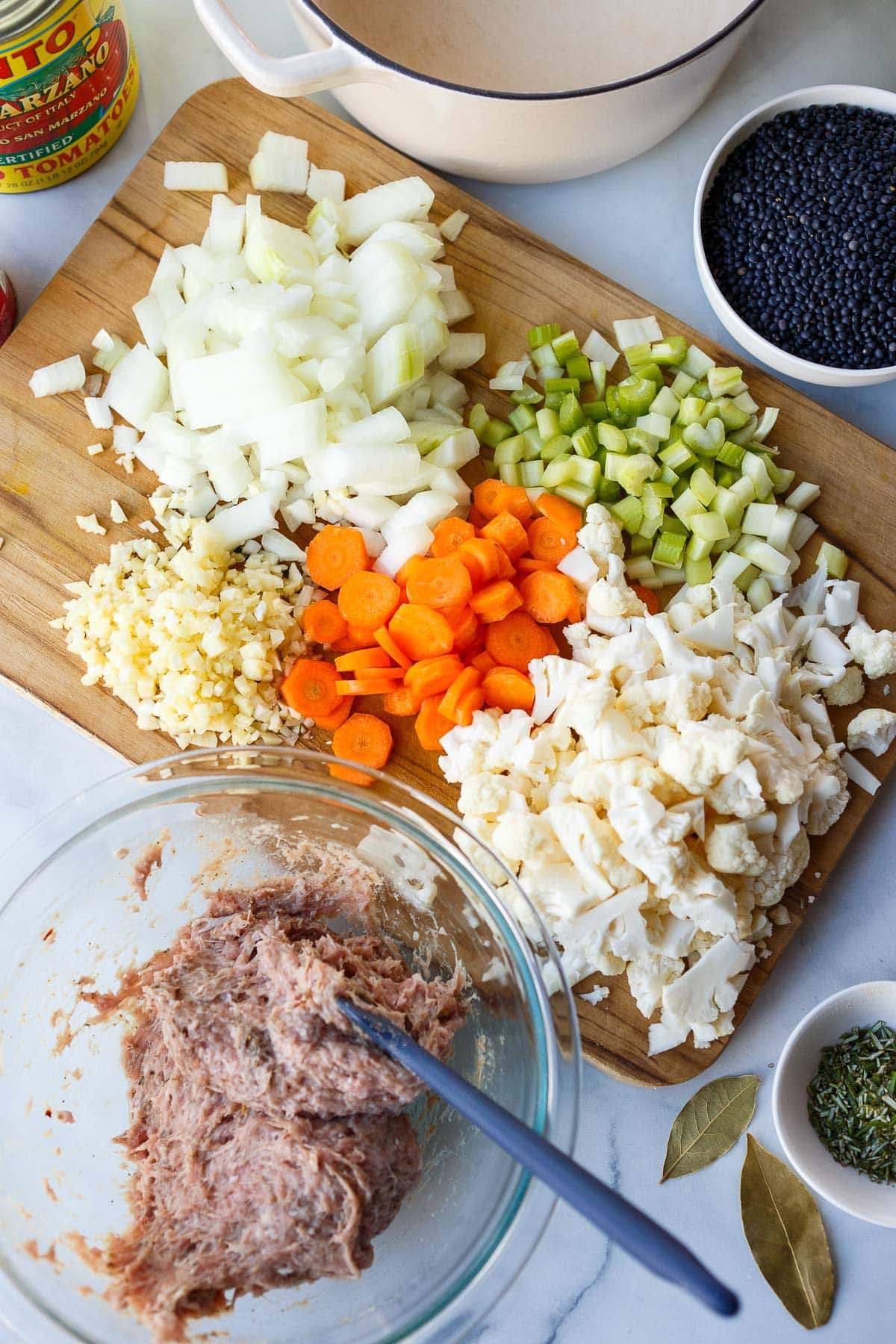 wood board with prepped veggies next to bowl with ground turkey mixed with spices using spatula.