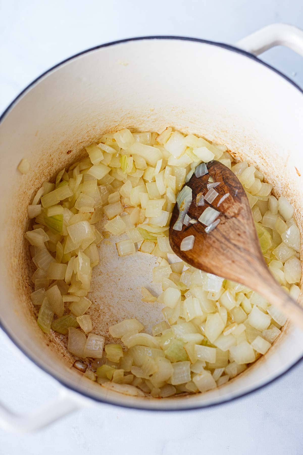 dutch oven with sautéed onions and wood spoon stirring.