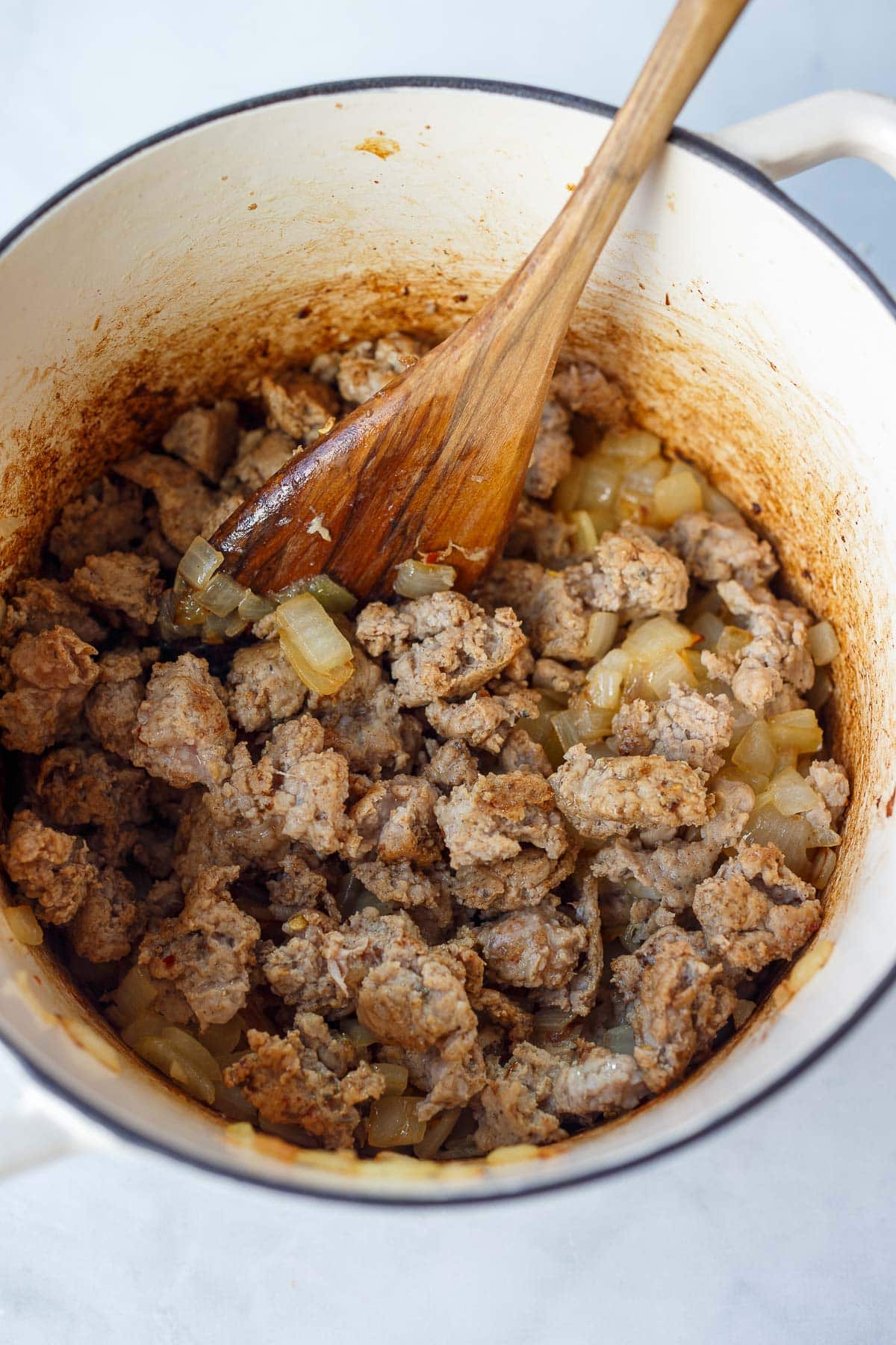 dutch oven with wood spoon stirring ground turkey with onions.