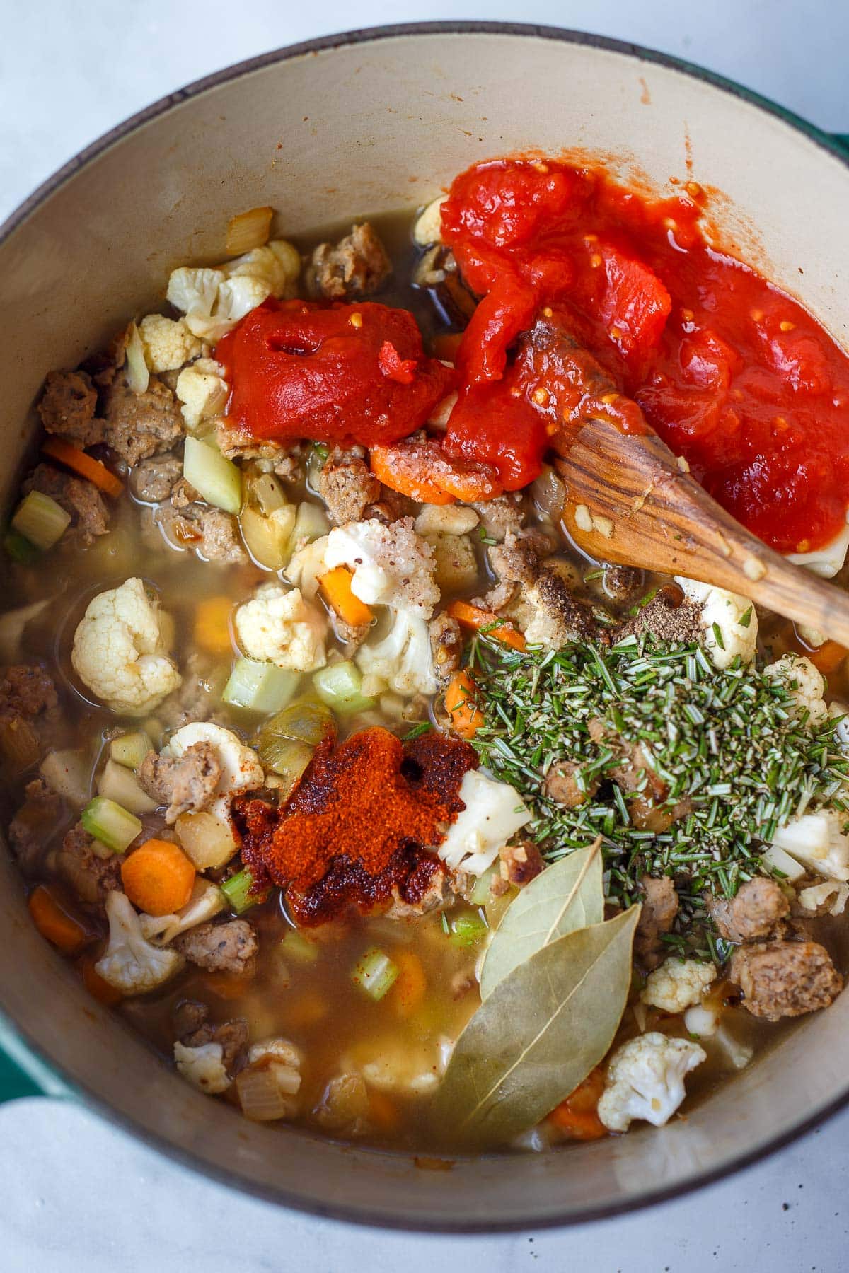 large pot of turkey sausage soup with tomatoes and spices added to the pot.