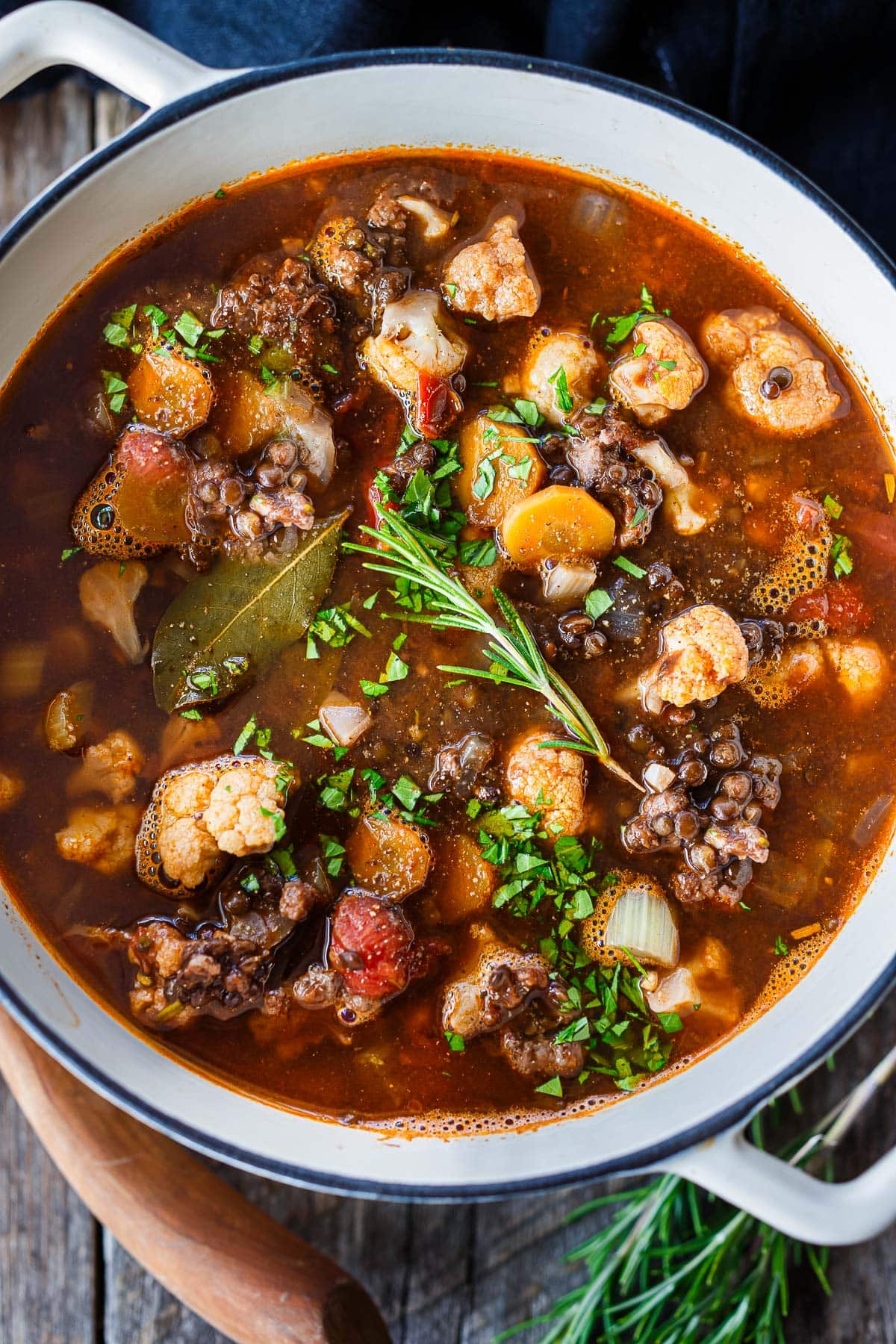 large pot with lentil turkey sausage soup topped with sprig of rosemary and minced parsley.