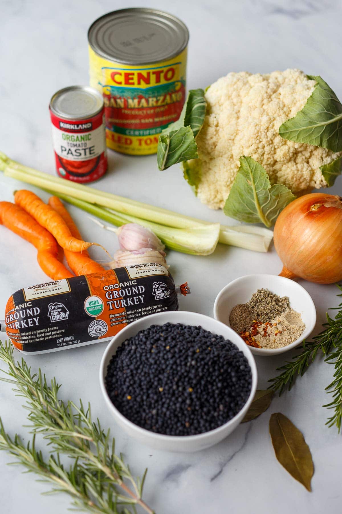 ingredients laid out for lentil turkey sausage soup - tomato paste, san marzano tomatoes, cauliflower, onion, celery, carrots, garlic, ground turkey, spices, lentils, rosemary, bay leaf.