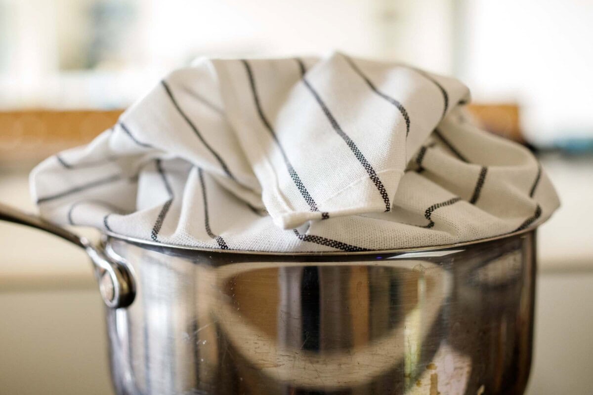 striped kitchen towel wrapped around the lid of a pot and placed on top to create a tight seal. 
