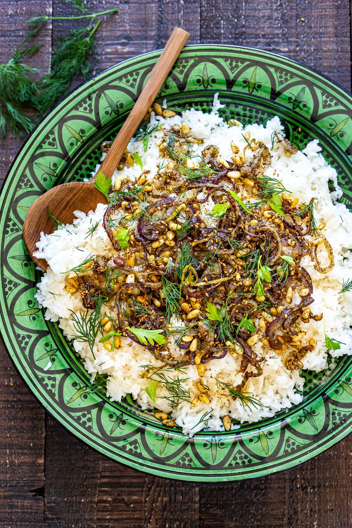 round green serving dish with middle eastern rice topped with shallots, lemon zest, zaatar, pine nuts, and herbs. 