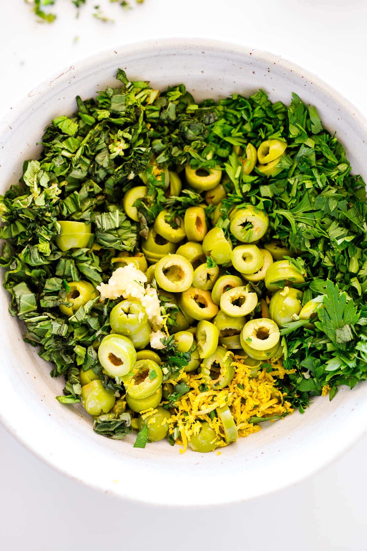 all the tapenade ingredients  in  a white bowl, ready to mix. 