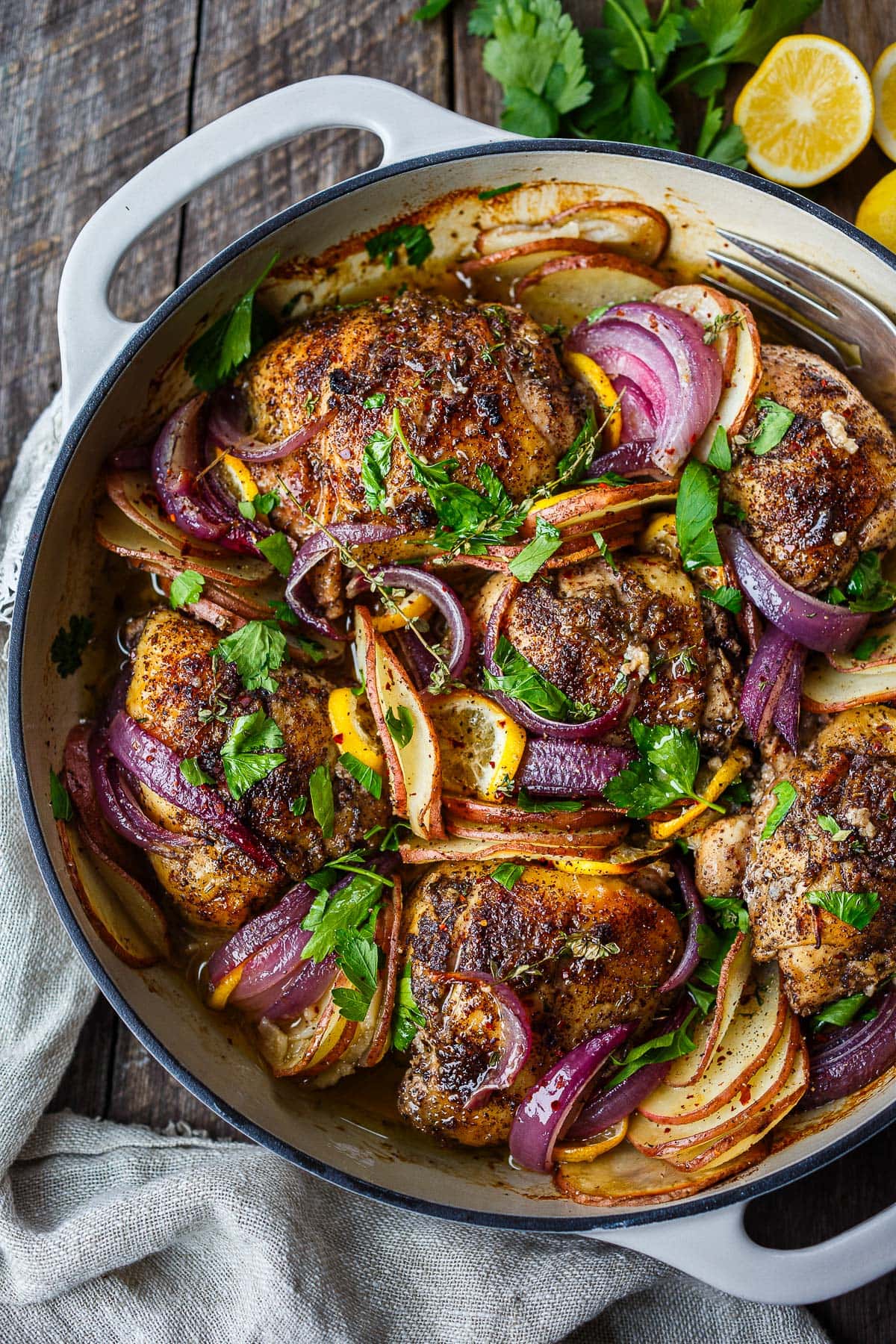 dutch oven with roasted chicken with sumac, sliced onions, potatoes, and meyer lemons tucked in between, fresh parsley and thyme over top.