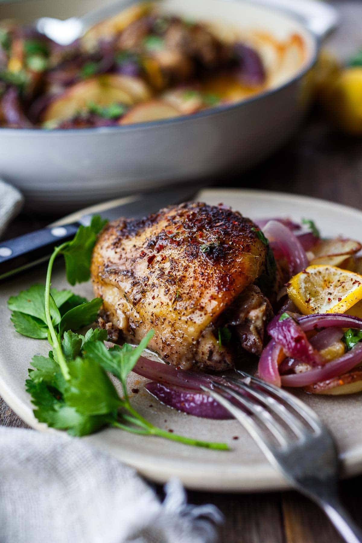 roasted sumac chicken thigh on a plate with sliced potatoes, onions, and meyer lemon, garnished with parsley.