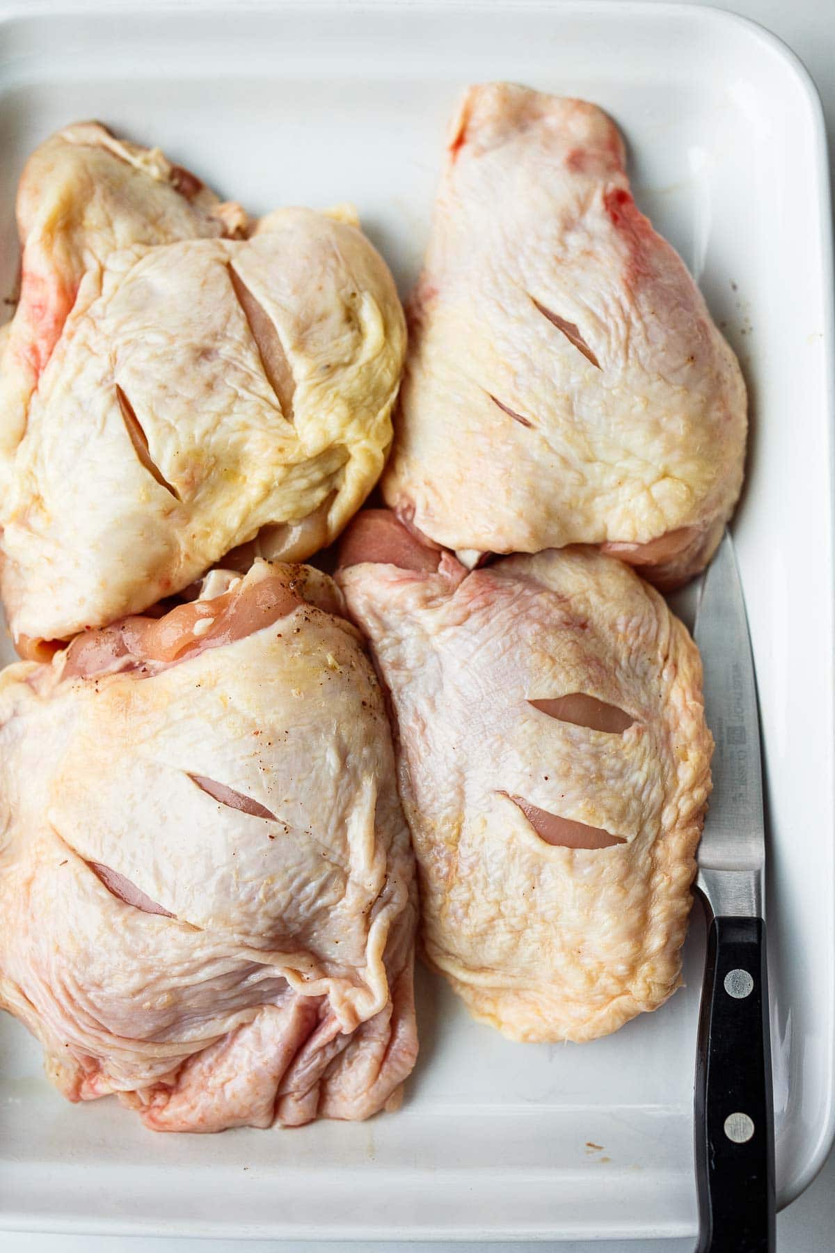 Raw chicken thighs on a tray with slits cut into the skin.