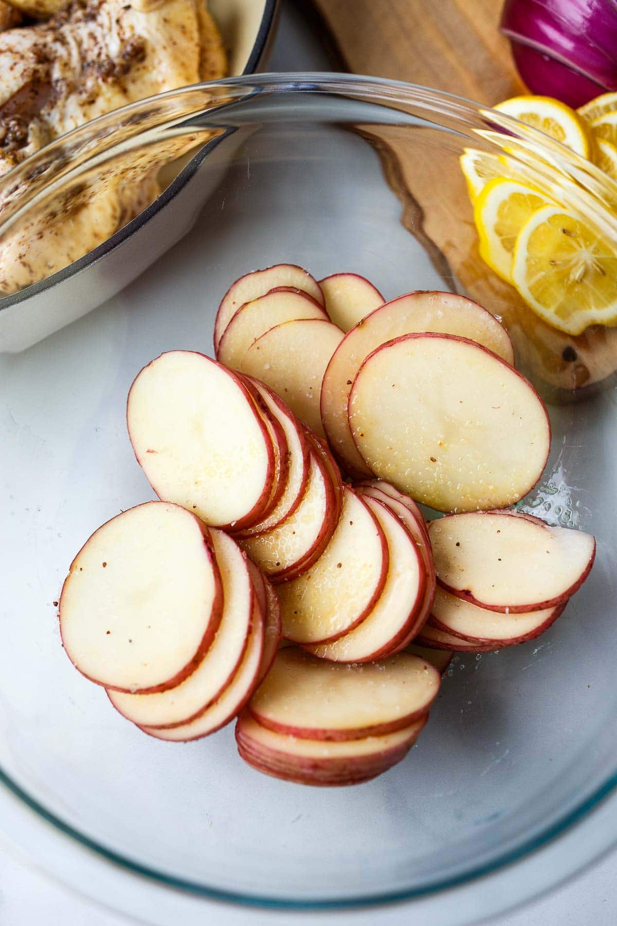 Potato slices in a glass bowl with olive oil and salt.