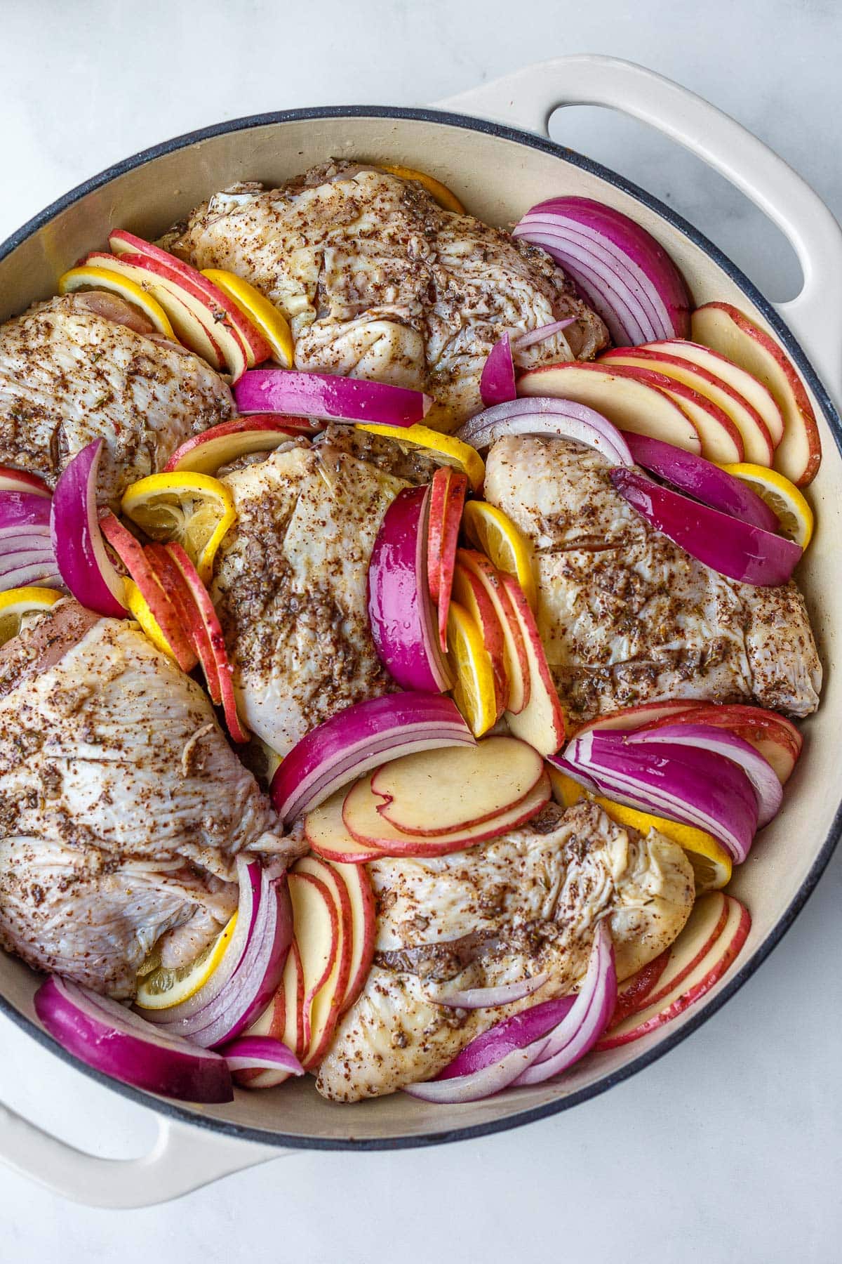 dutch oven with chicken thighs and sliced potatoes, onions, and lemons tucked in between.