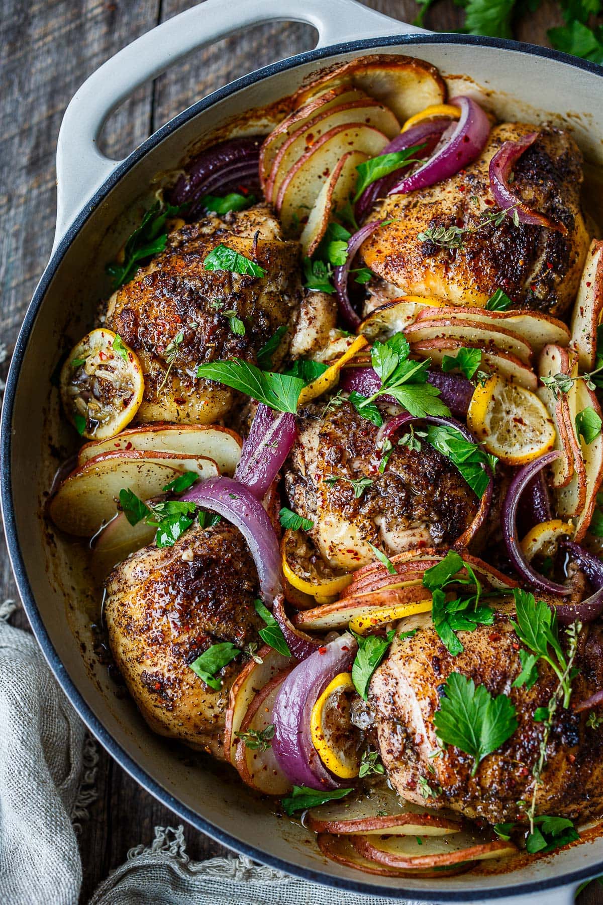 braiser filled with roasted sumac chicken, lemons and sliced potatoes and red onions, garnished with fresh herbs.