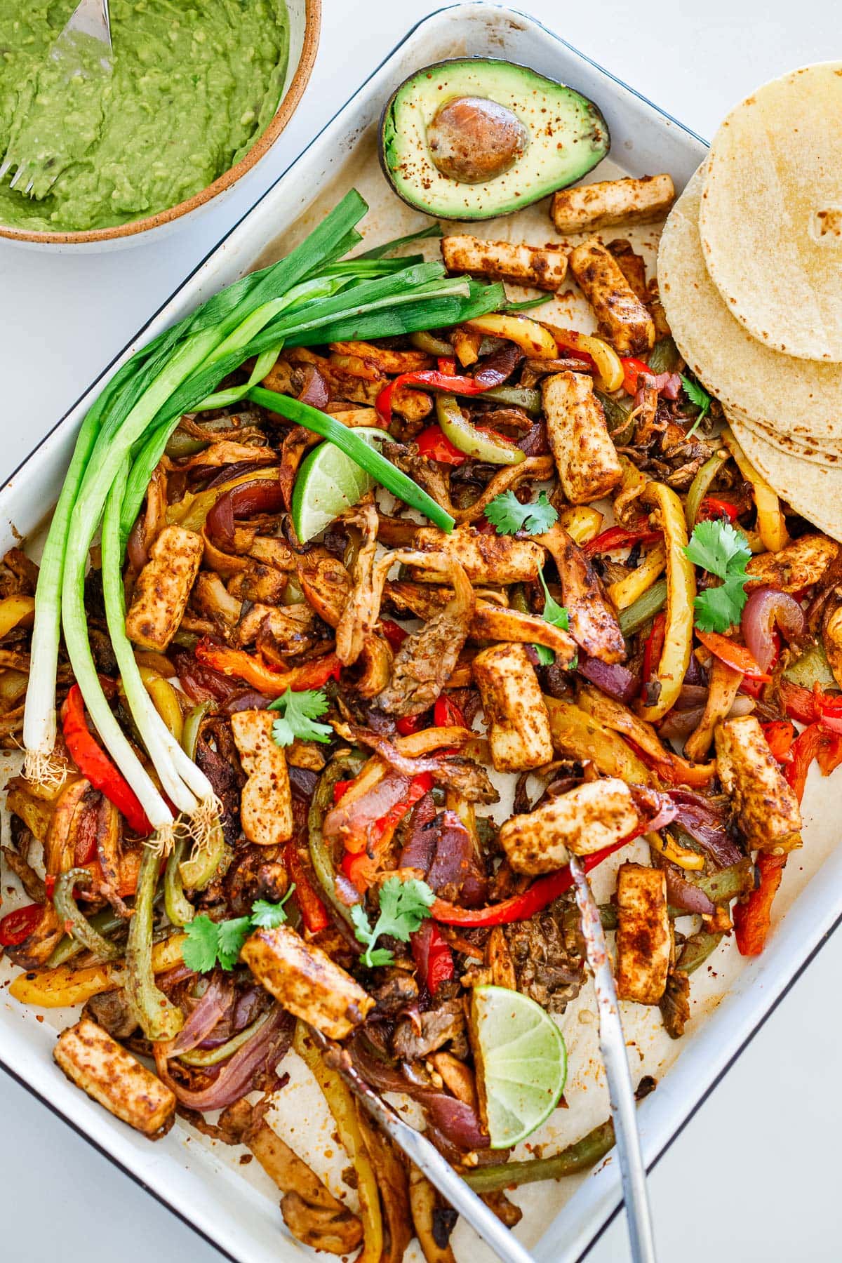 sheet pan with vegan fajitas and tofu and oyster mushrooms with lime wedges, green onions, and tortillas. 