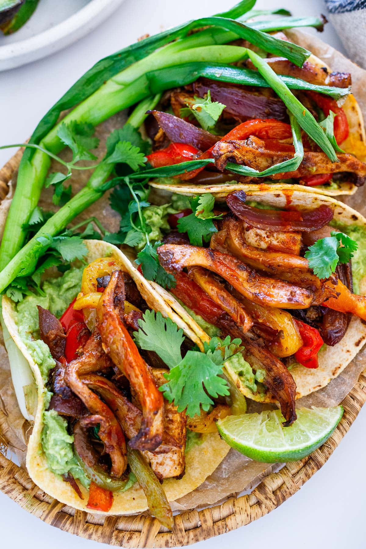 vegan fajitas made with oyster mushrooms, onions, and peppers stuffed into tortillas with mashed avocado, topped with cilantro. 