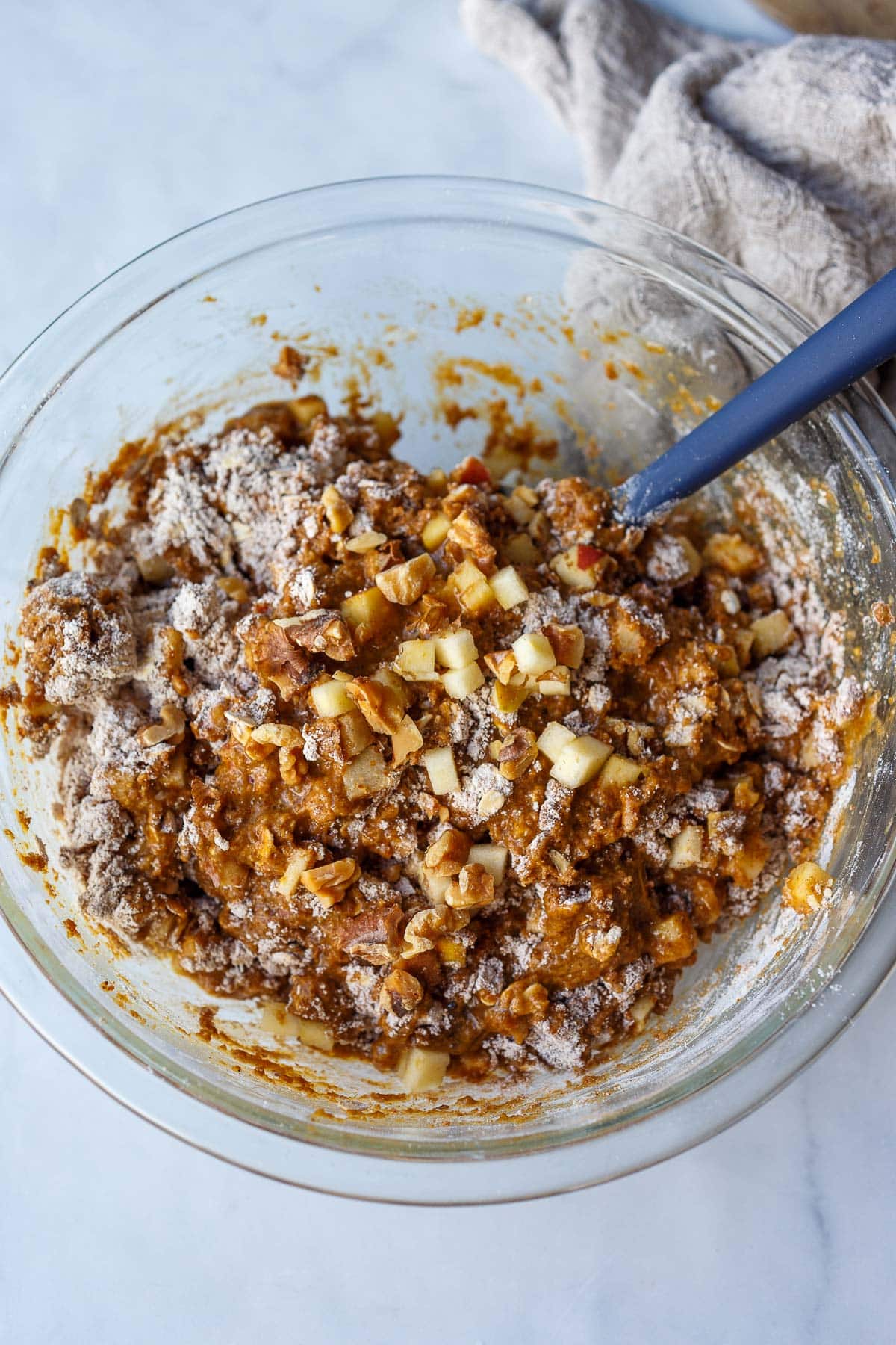 large glass bowl with apple oat muffin batter and spatula mixing.