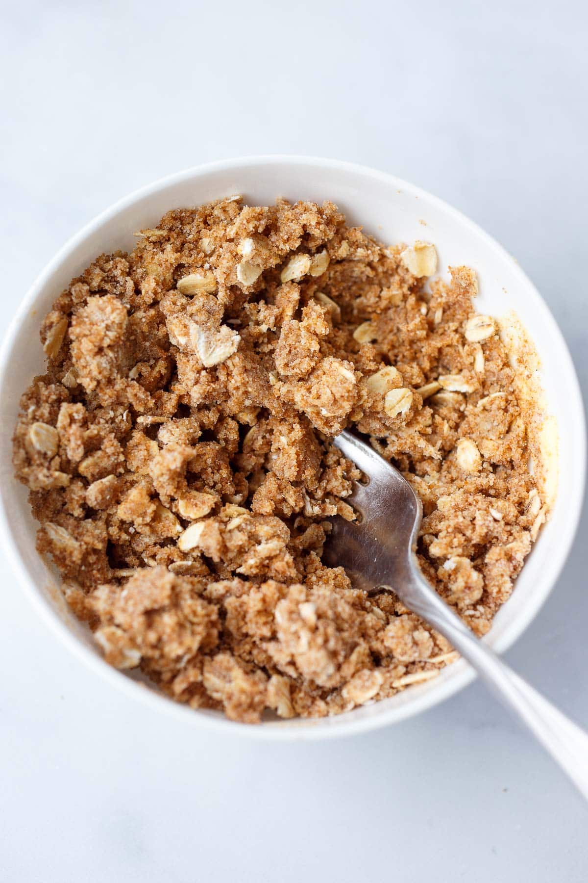 small bowl with fork mixing apple oat muffin crumble topping.