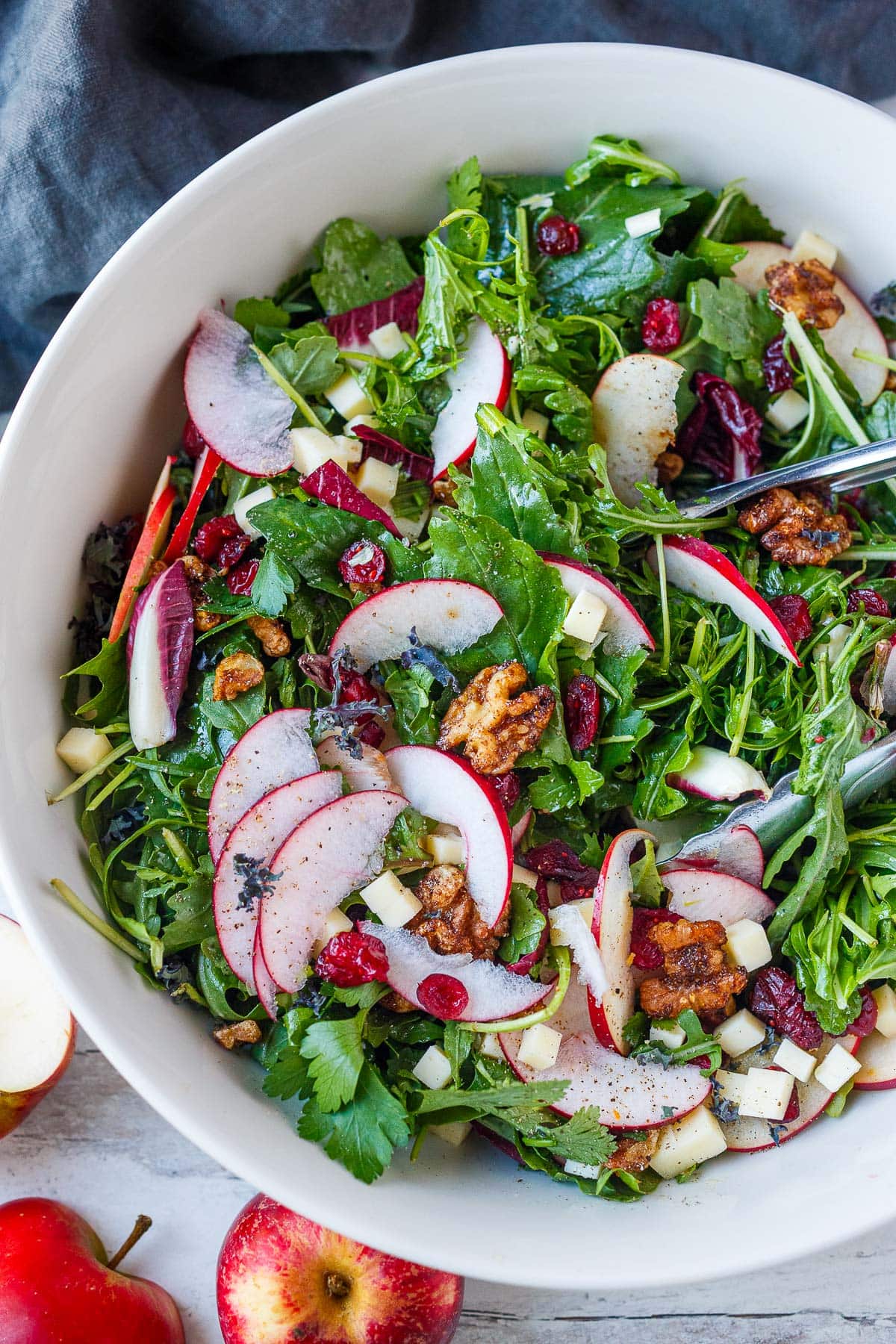 apple cheddar salad with cinnamon walnuts in large bowl with tongs.