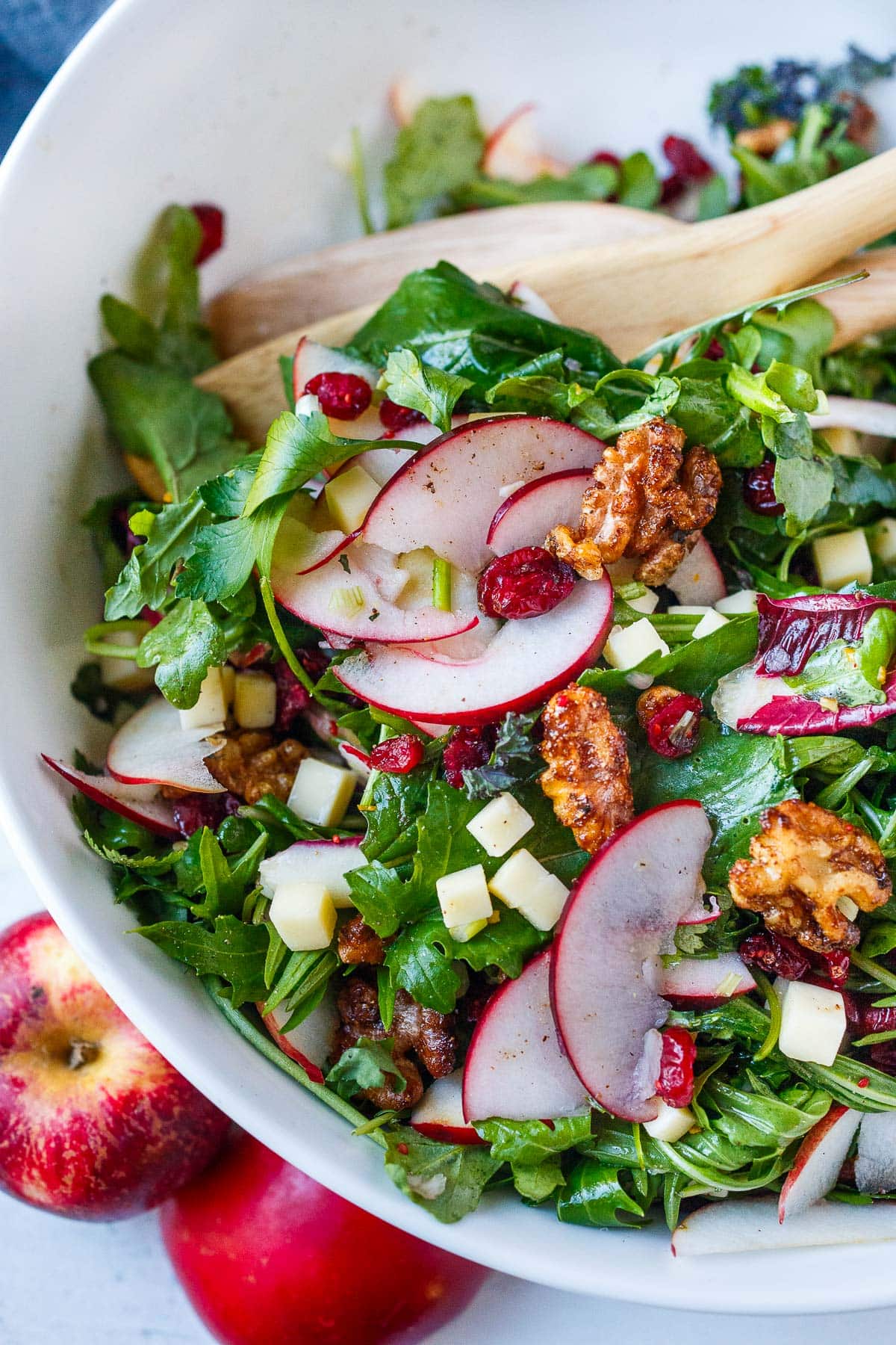 apple cheddar salad with cinnamon walnuts in serving bowl with wood spoons.