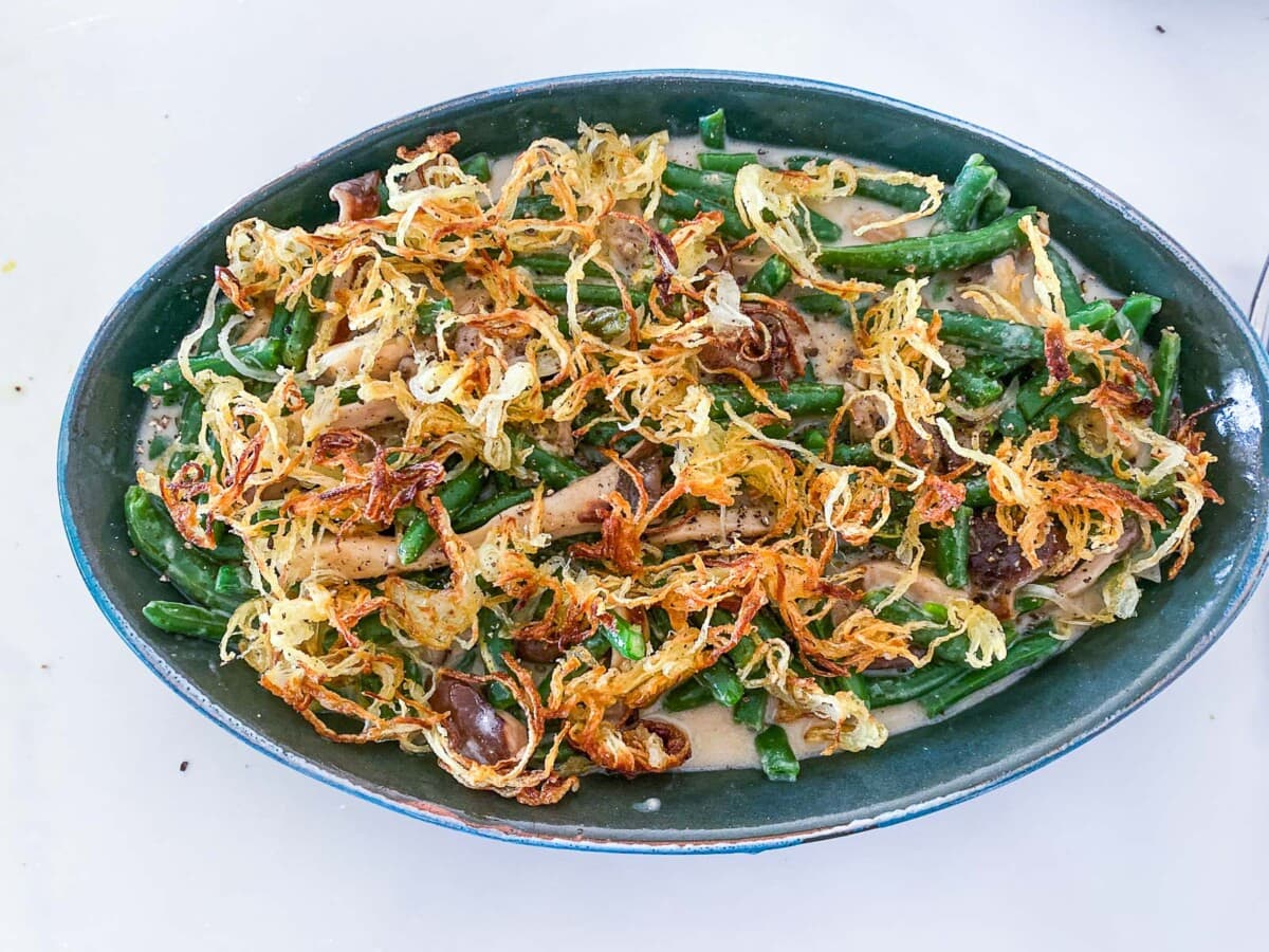 green bean casserole with crispy onion topping in oval baking dish.