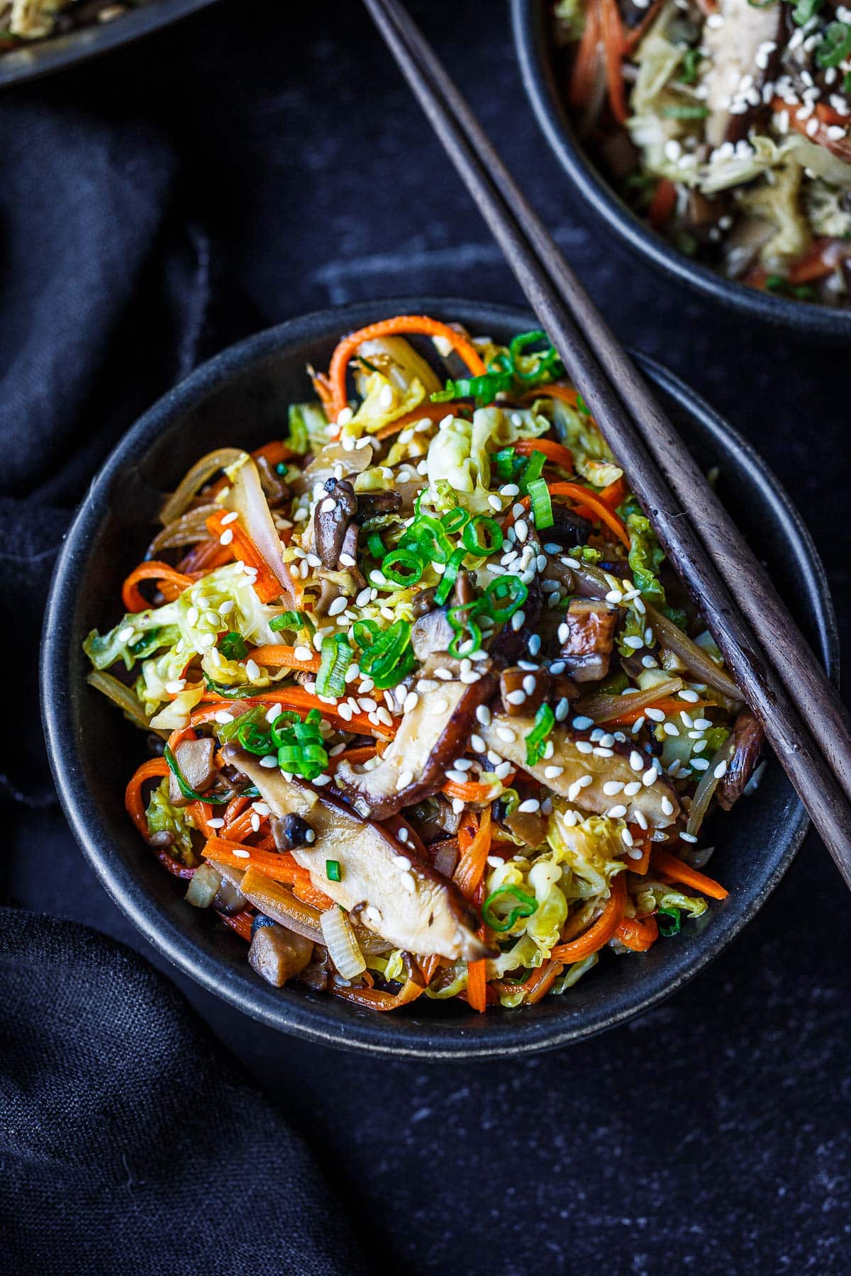 deconstructed egg roll in a bowl garnished with sesame seeds and green onions with chopsticks on top.
