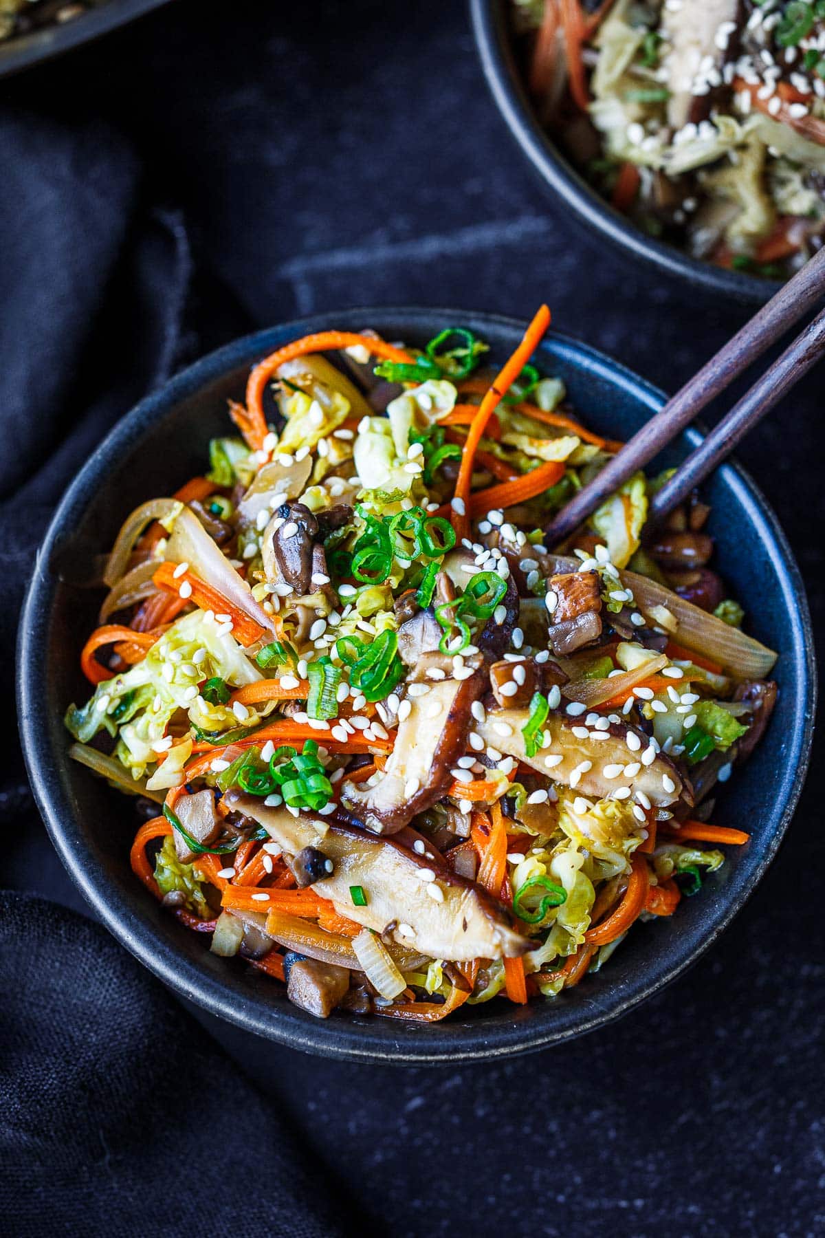 egg roll in a bowl garnished with sesame seeds and green onions with chopsticks.