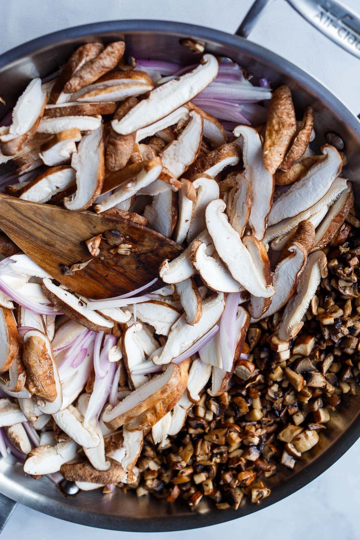 large skillet with wood spoon stirring sliced shallots and mushrooms.