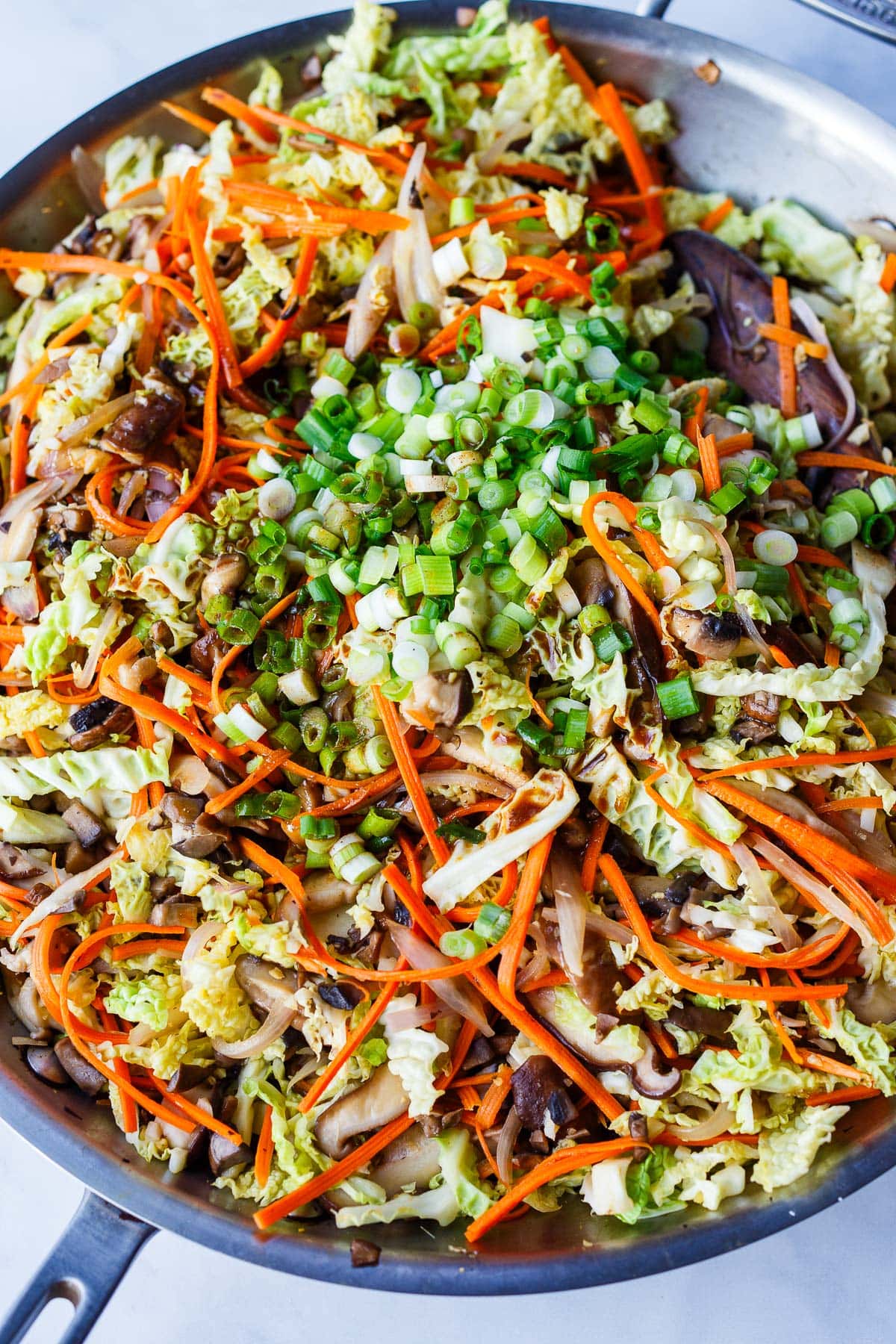 large skillet with deconstructed egg roll in a bowl topped with chopped green onions and stir fry sauce.