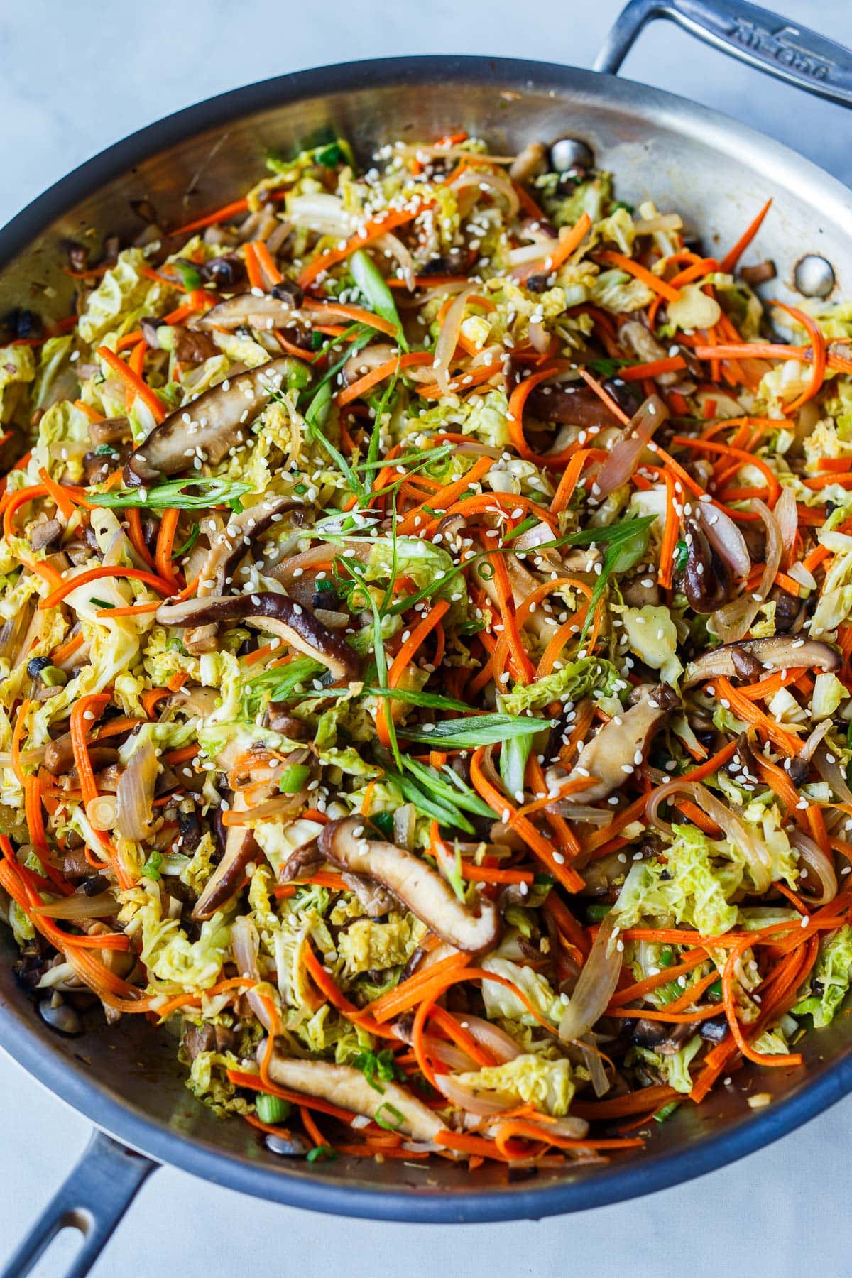 large skillet with deconstructed egg roll in a bowl with green onions and toasted sesame seeds.