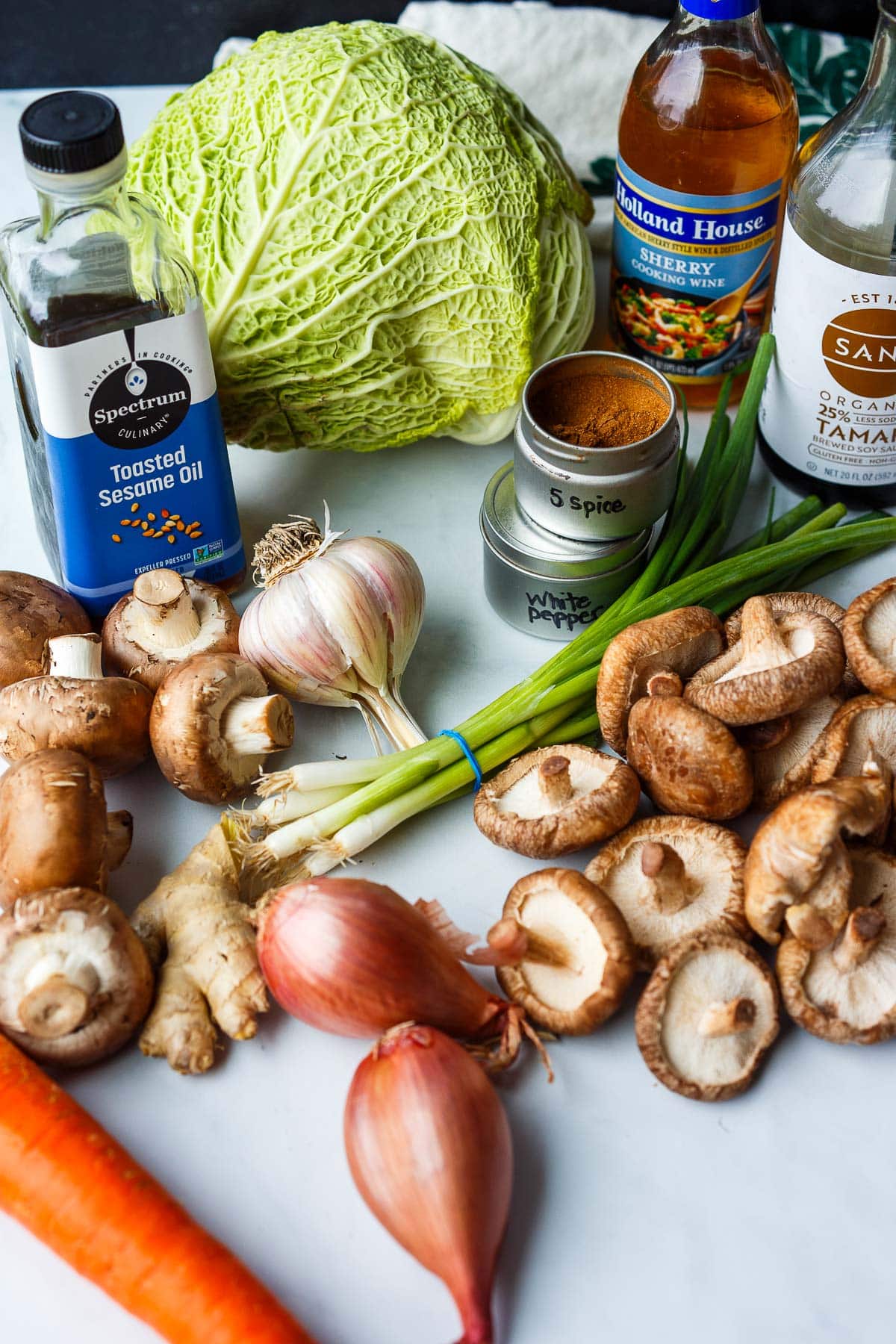 ingredients for egg roll in a bowl laid out - savoy cabbage, sherry cooking wine, tamari, toasted sesame oil, spices, green onions, garlic, mushrooms, shallots, carrot.