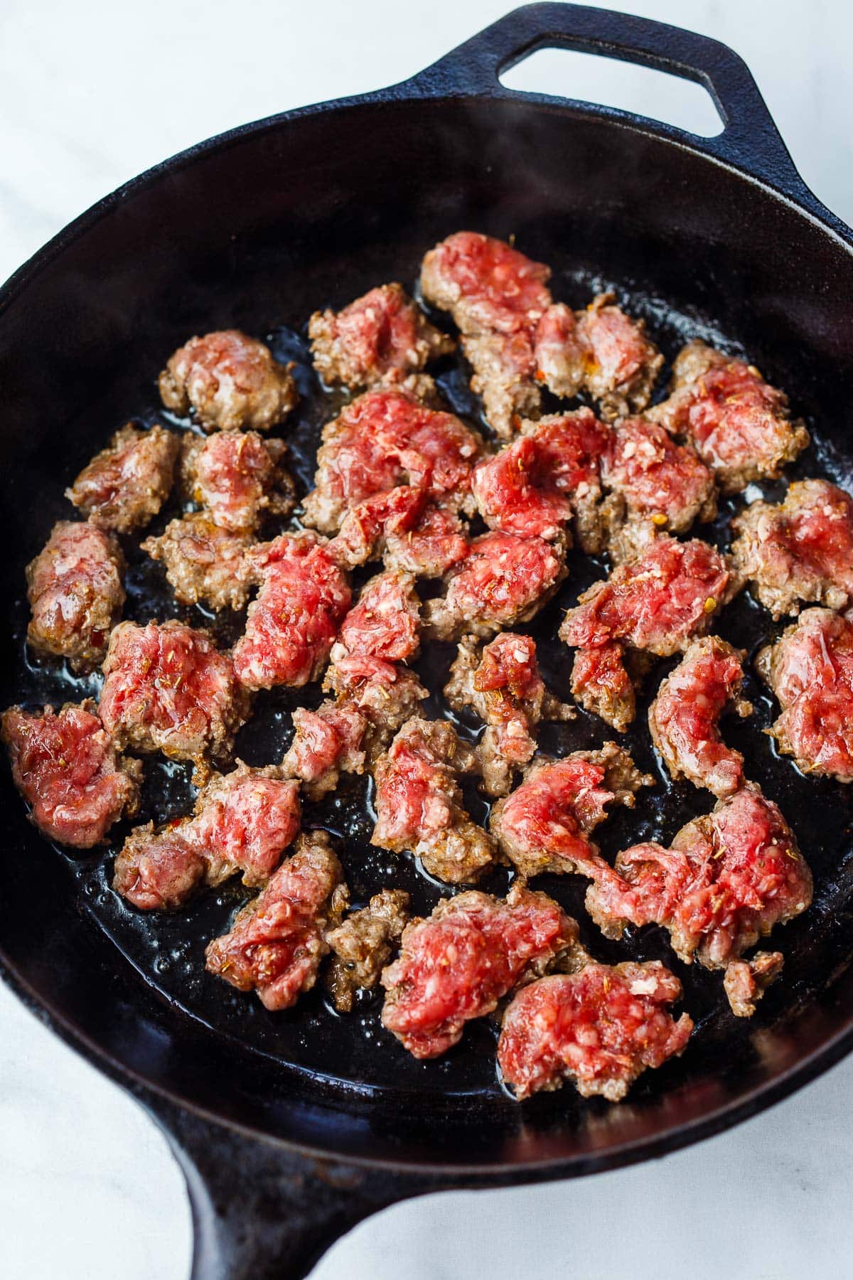 Italian sausage broken into crumbles, cooking in cast iron skillet. 