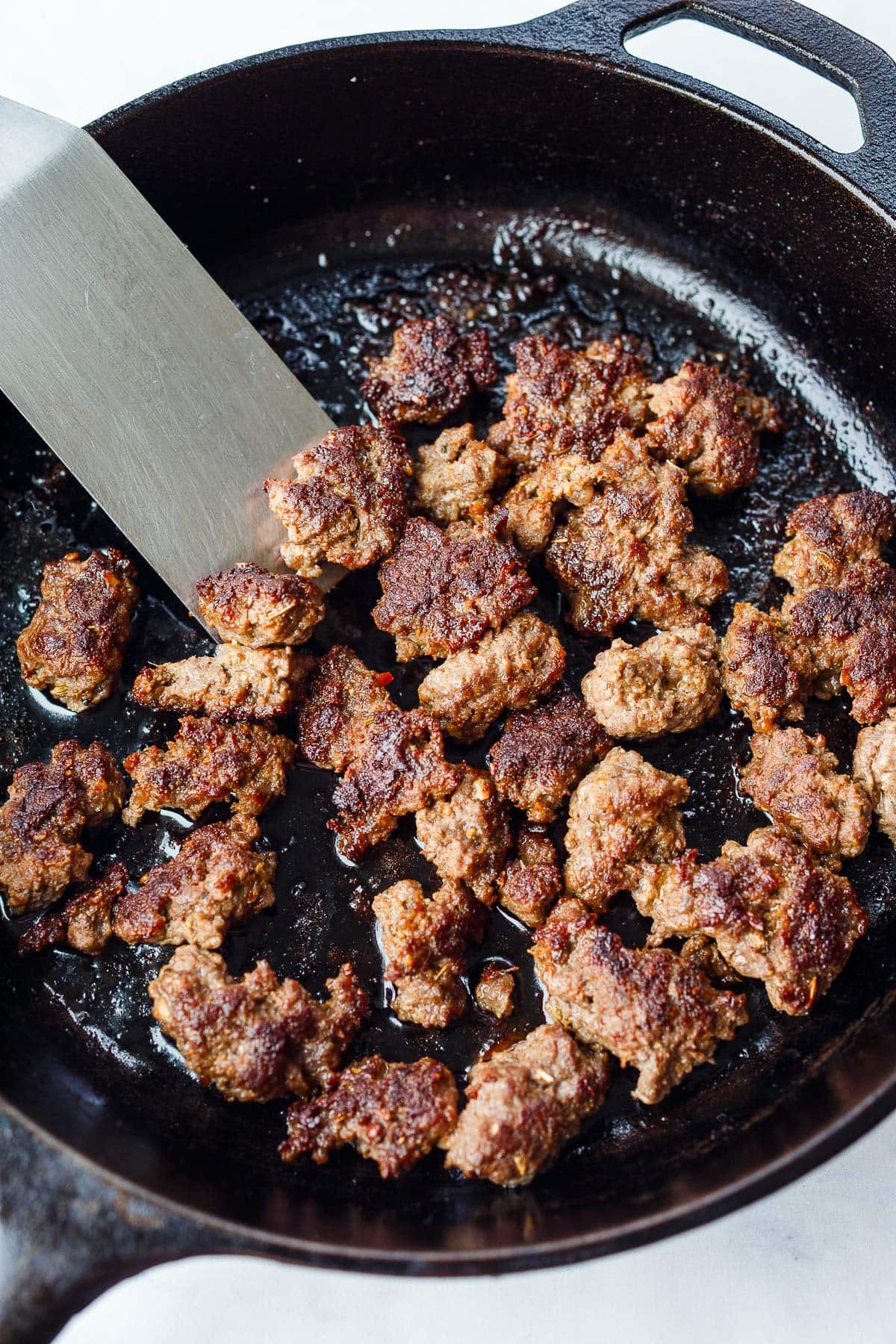 Cooked sausage crumbles in a cast iron pan.