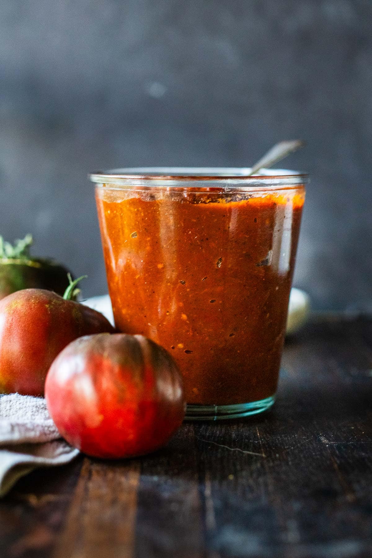 jar of homemade ketchup next to garden fresh tomatoes.