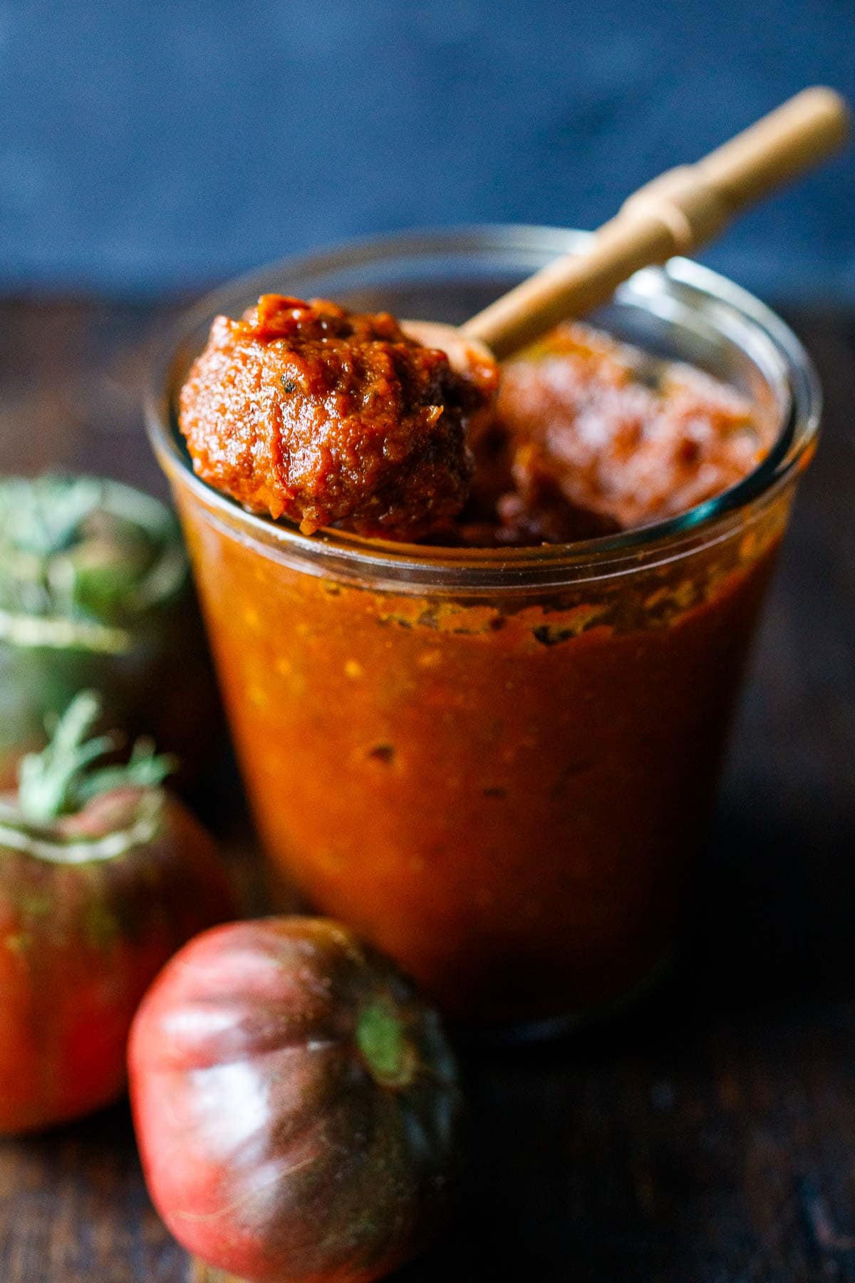 wood spoon holding spoonful of homemade ketchup above jar.